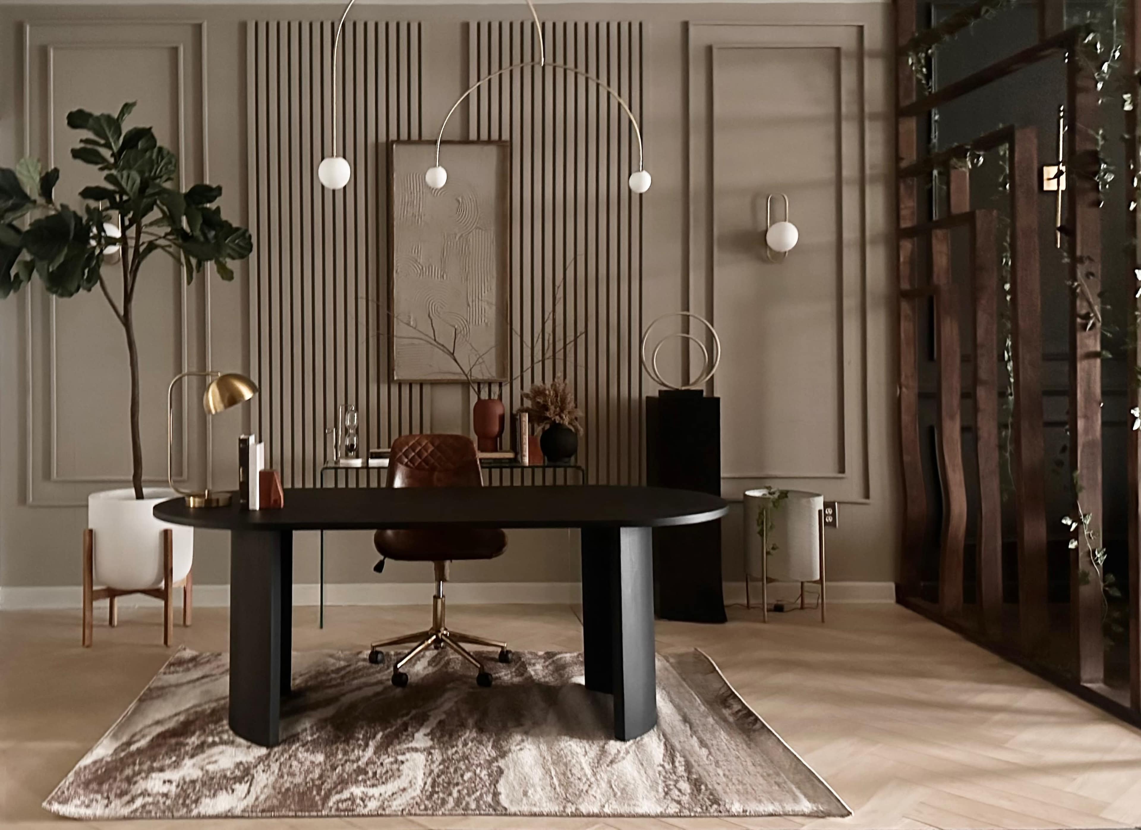 A modern office space features a round black desk with a brown office chair, surrounded by decorative plants and geometric wall panels.