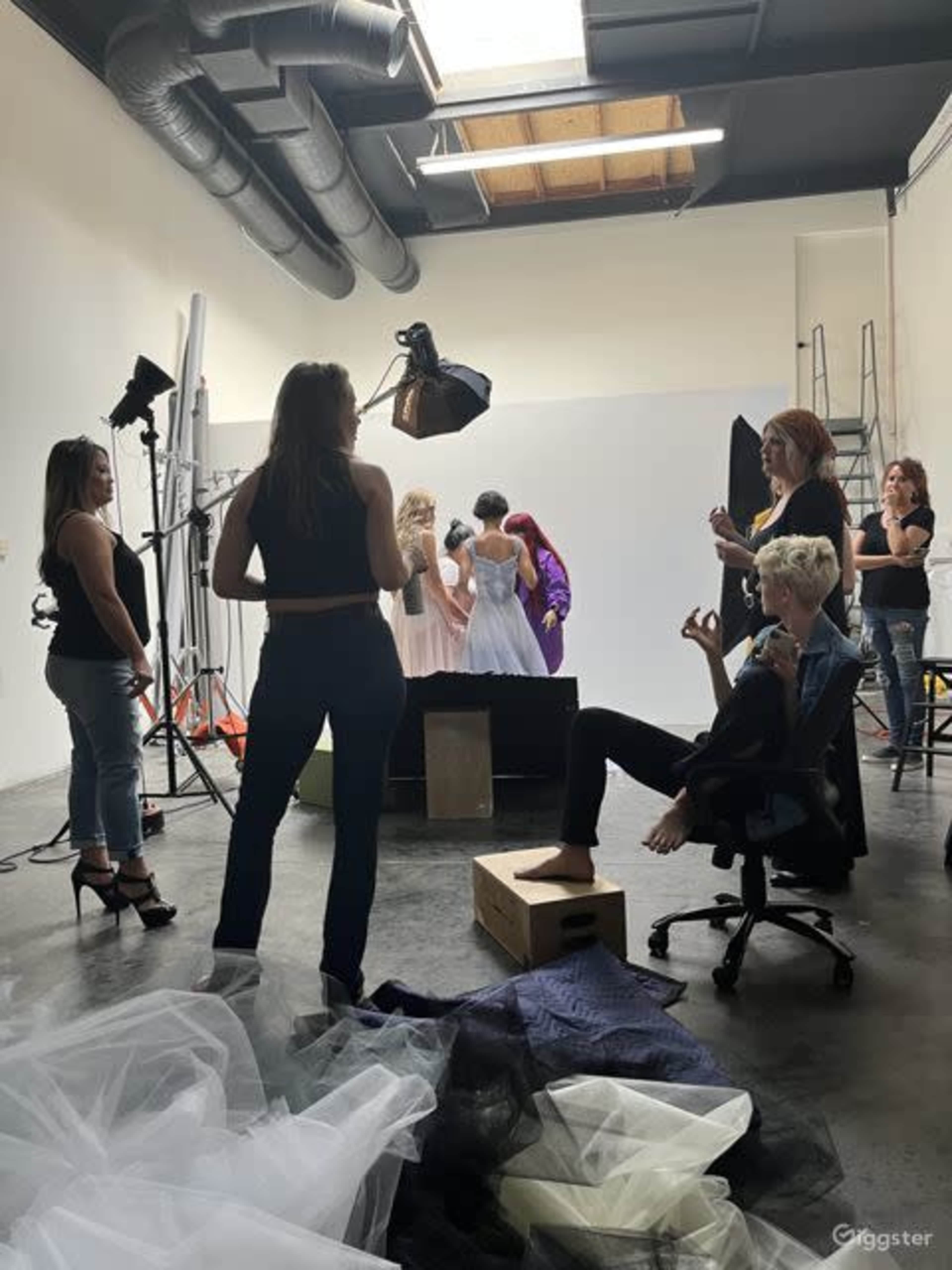 A group of people works in a studio setting, with some preparing for a photo shoot while others pose in elegant dresses.