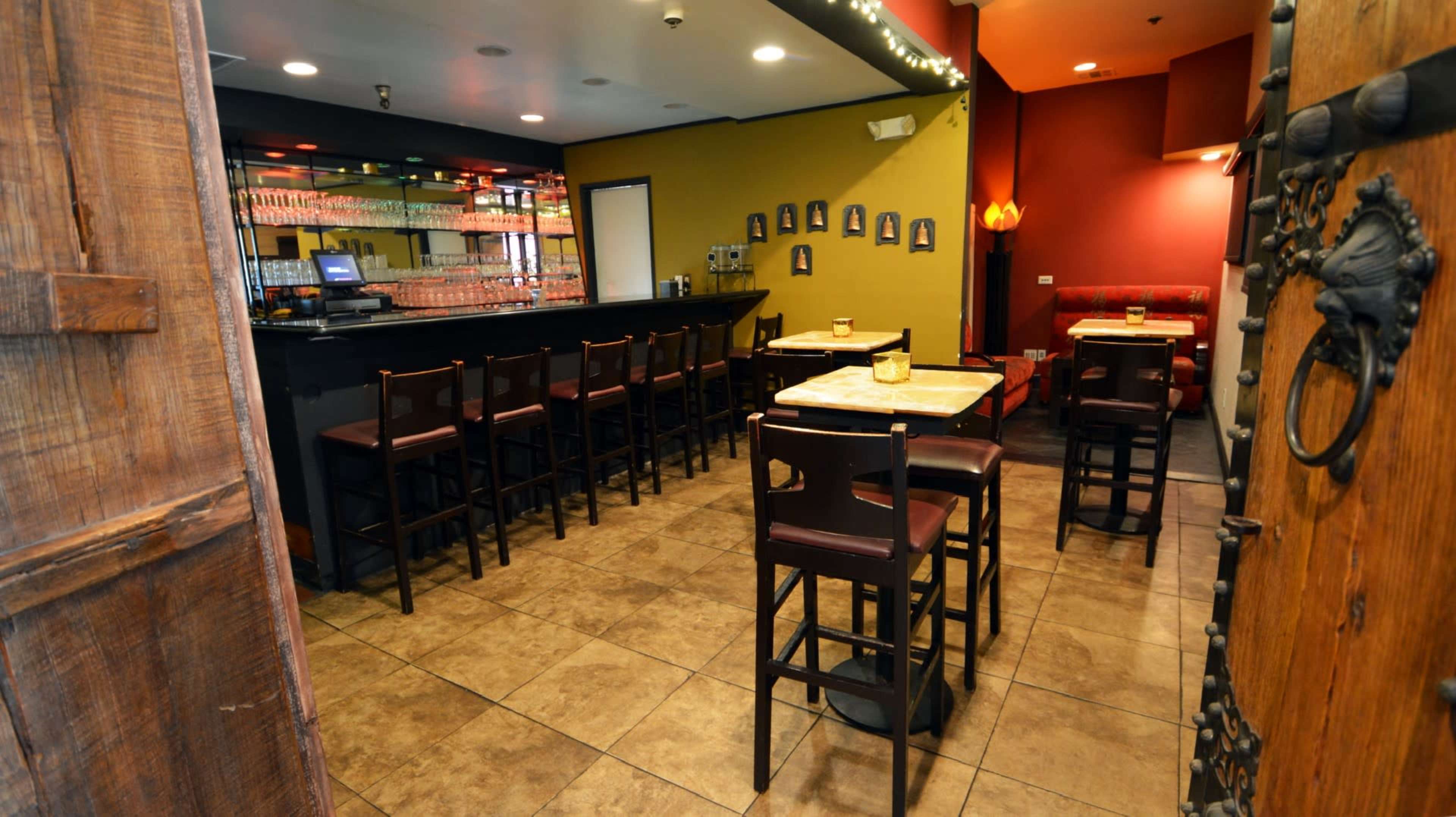 The image shows the interior of a bar featuring a long counter with stools and several tables arranged on a tiled floor.