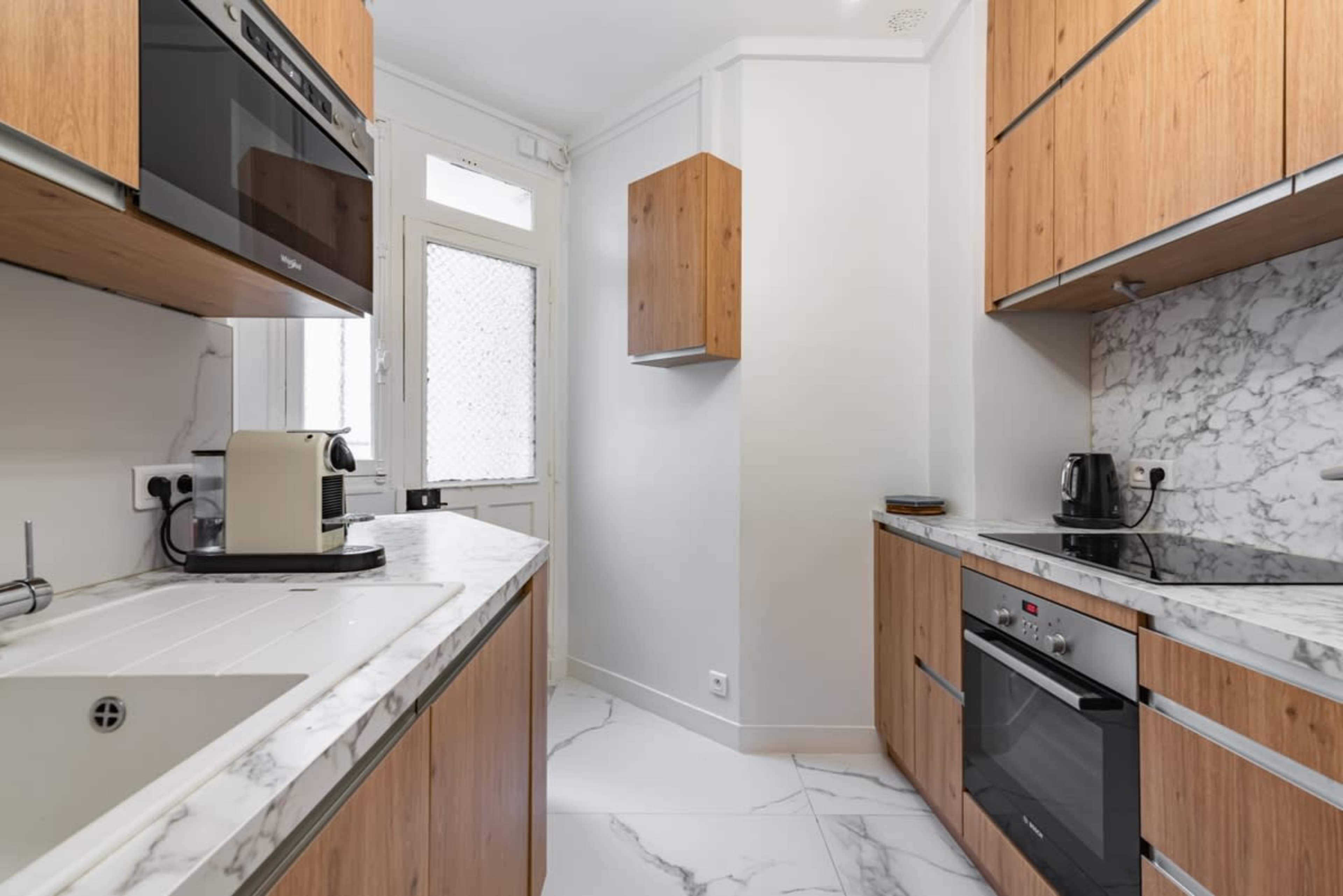 A modern kitchen features wooden cabinetry, marble countertops, and stainless steel appliances, with a window providing natural light.