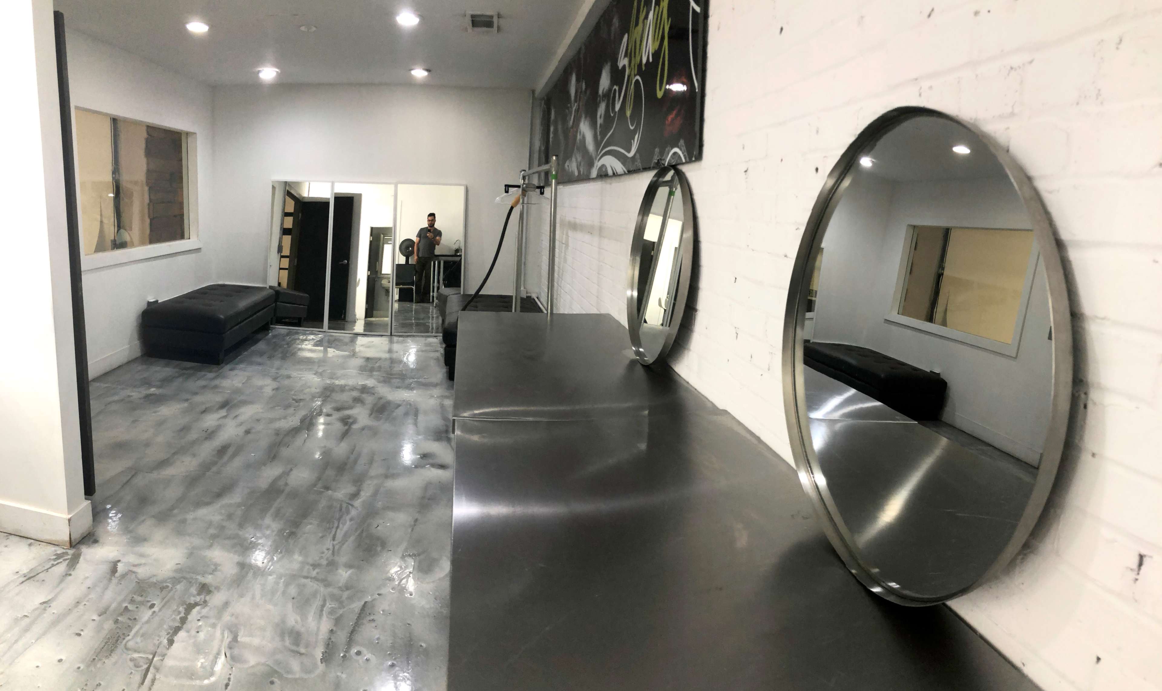A spacious, well-lit room with a polished concrete floor, mirrors mounted on a black countertop, and seating along the walls.