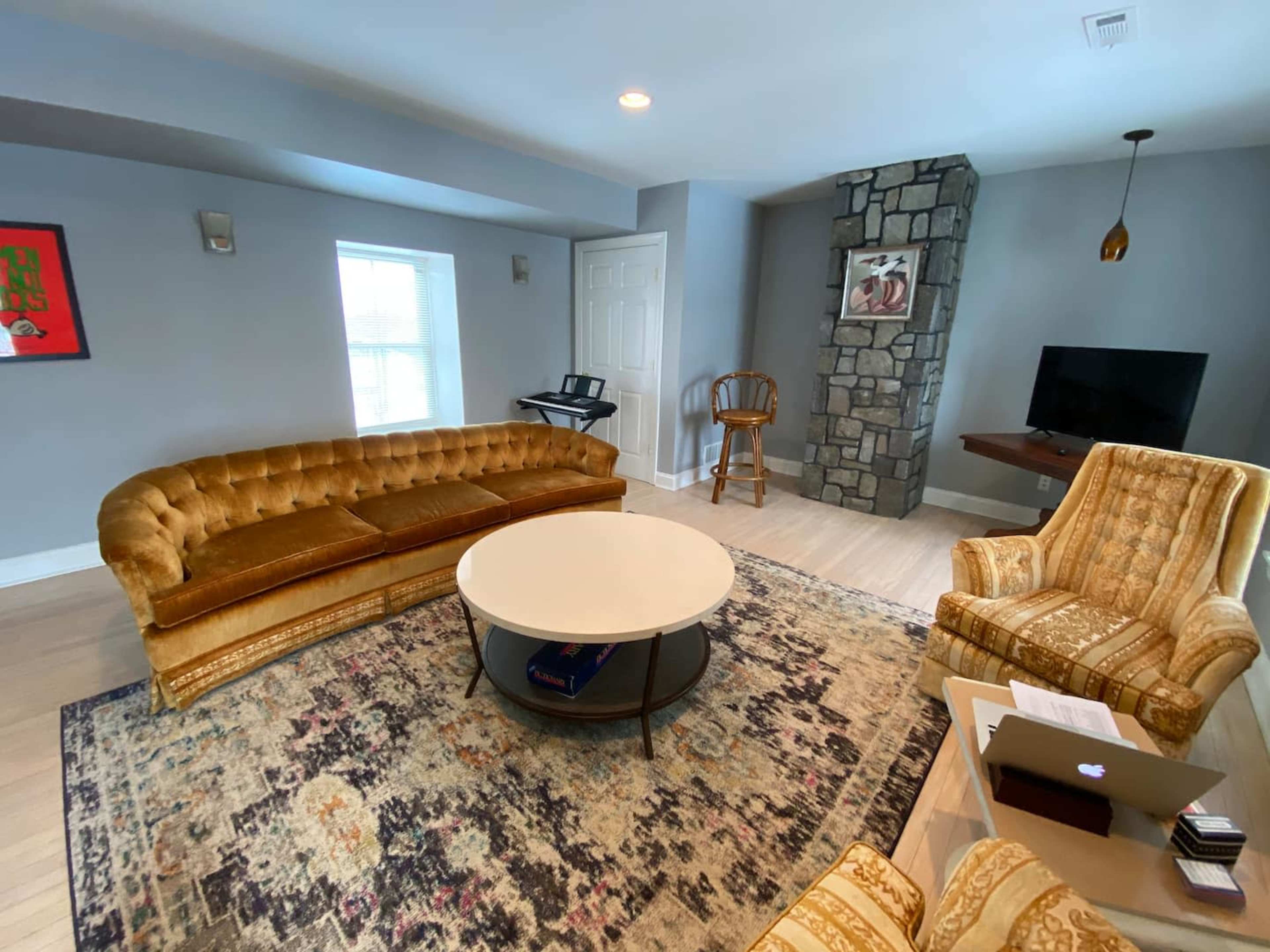 A modern living room featuring a circular coffee table, a yellow tufted sofa, two patterned armchairs, and a stone accent wall with a television.