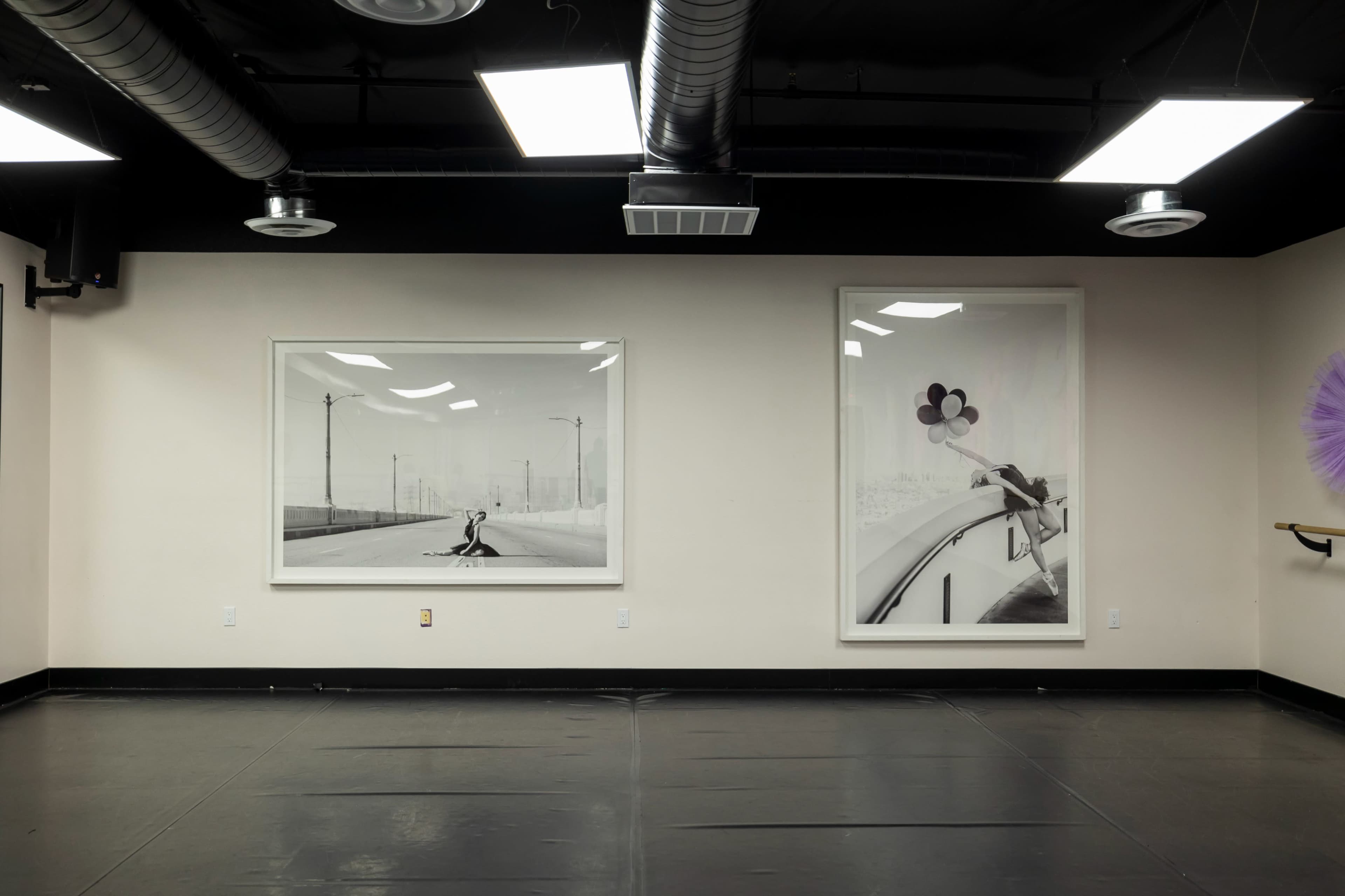 The image shows a dance studio with two large framed black-and-white photographs on the walls and a mirrored panel on the left side.