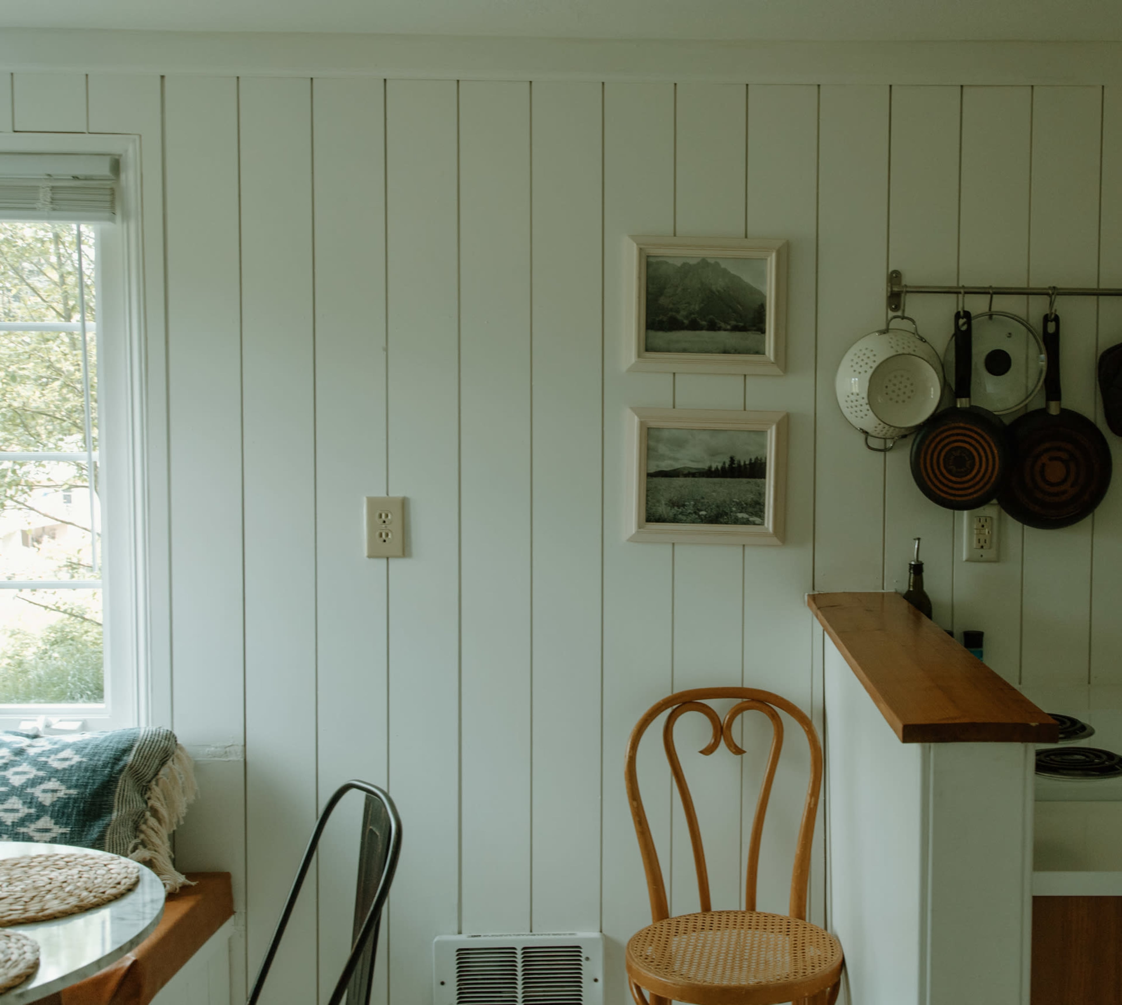 A pegboard displays cooking utensils while two framed pictures hang on a white-paneled wall in a calm kitchen space.