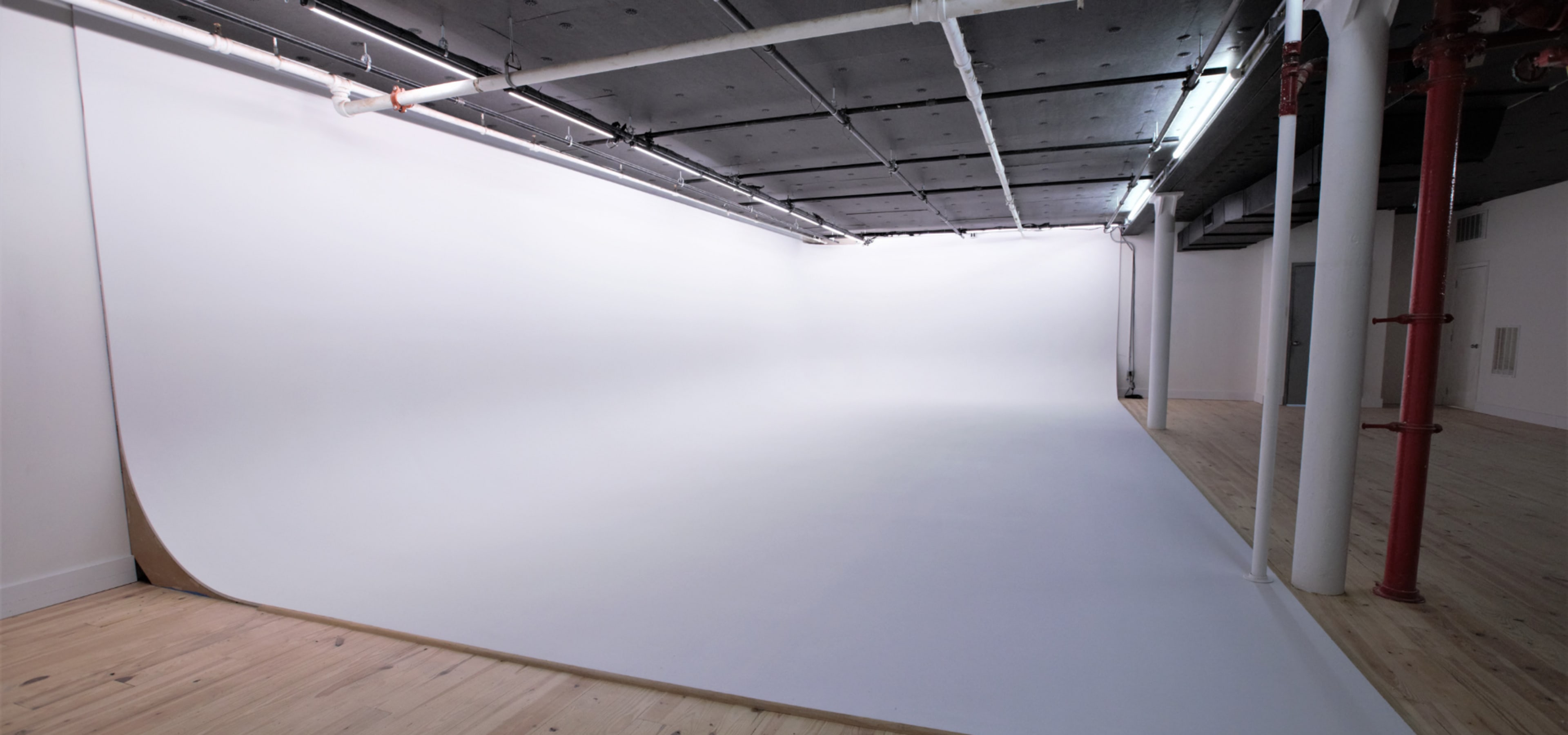 The image shows a spacious, empty photography studio with a seamless white backdrop and wooden flooring.