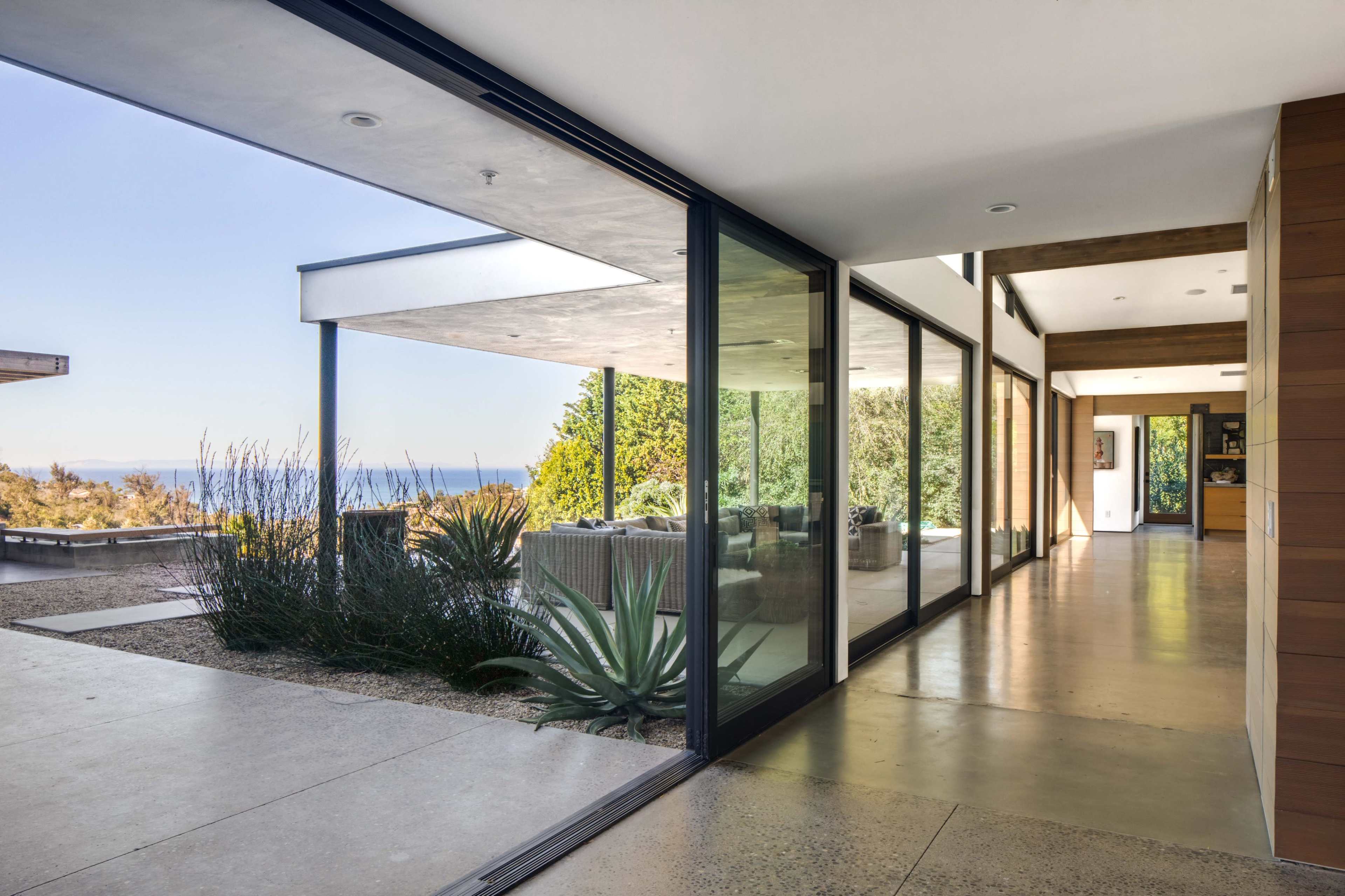 A modern hallway with large glass windows overlooks a landscaped area and a view of the ocean.