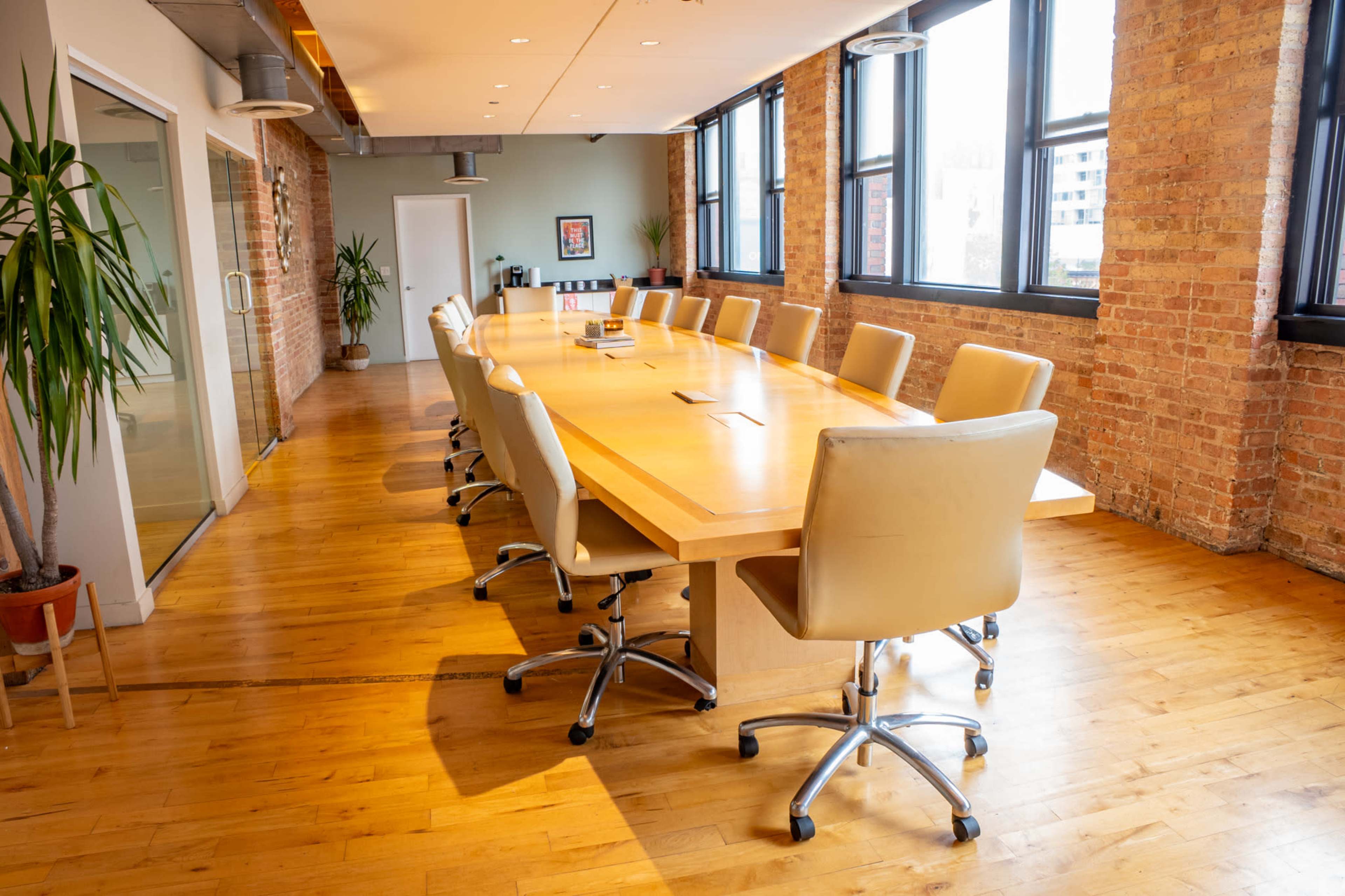 A spacious conference room features a long wooden table surrounded by leather chairs, with large windows allowing natural light to illuminate the space.