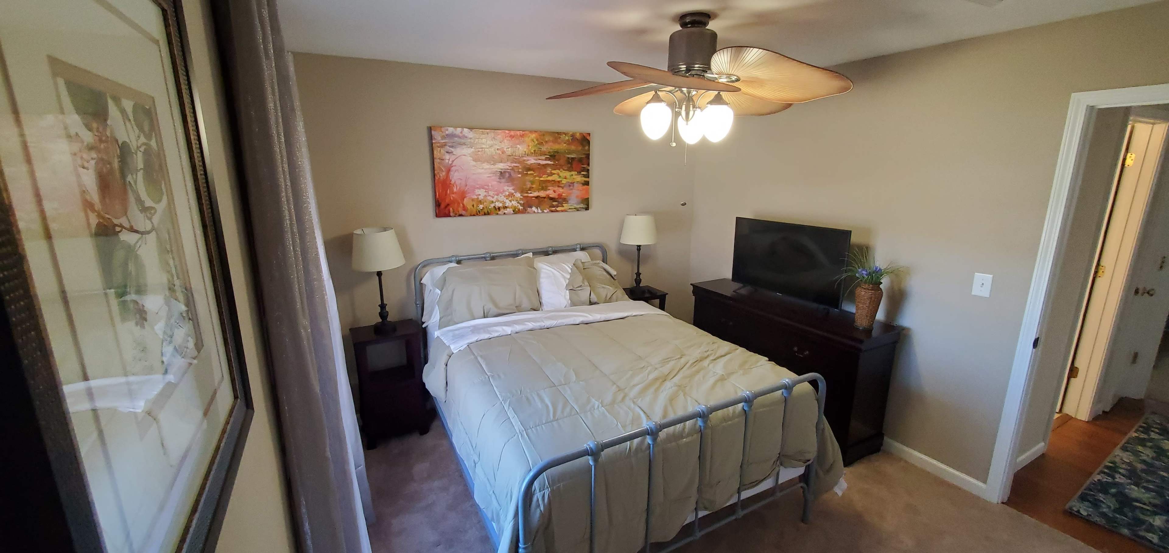 A bedroom with a metal bed frame, a television on a dresser, and two bedside lamps beside the bed.
