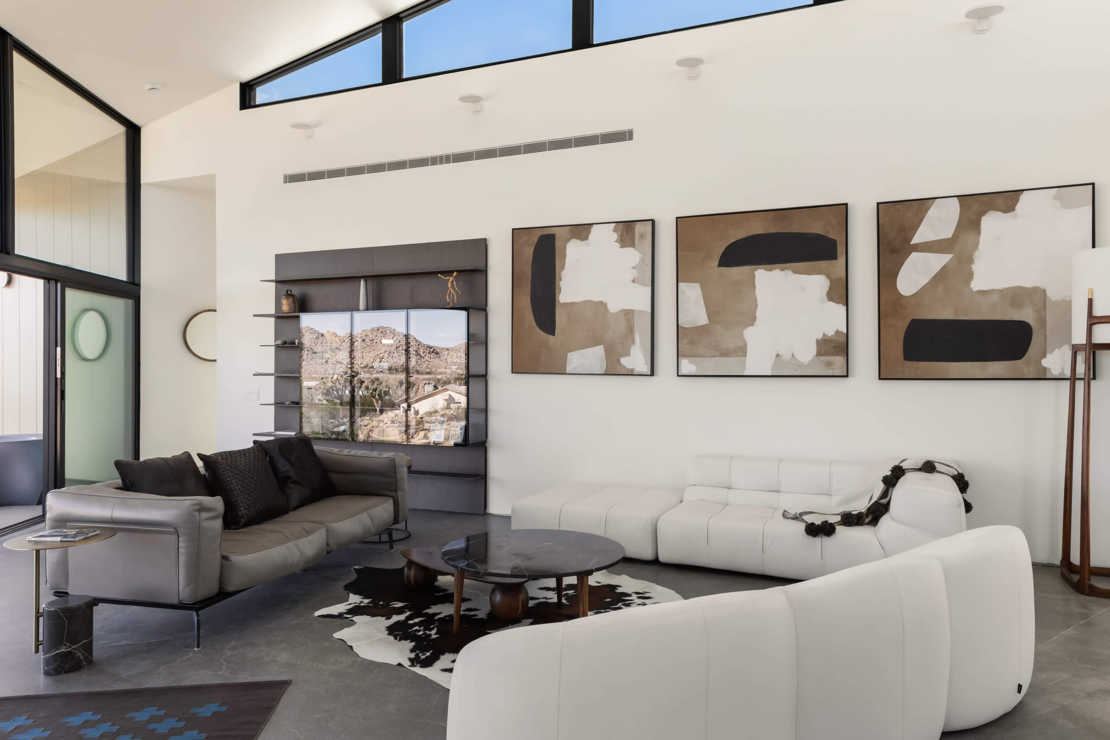 The scene shows a modern living room with large windows, minimalist furniture, and abstract artwork on the walls.