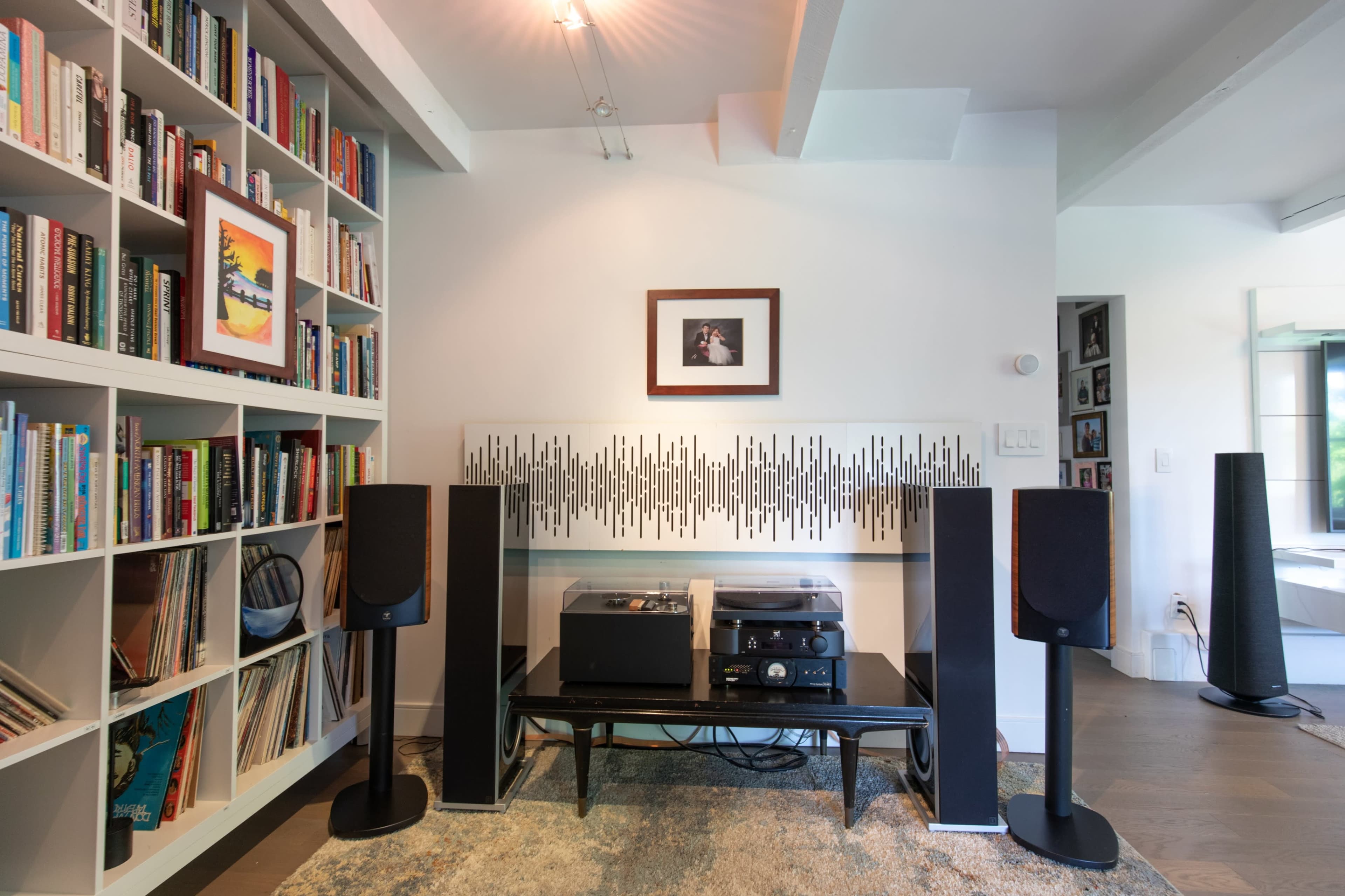 A modern living room features a sleek entertainment center with audio equipment flanked by tall speakers, alongside a bookshelf filled with books and framed artwork on the walls.
