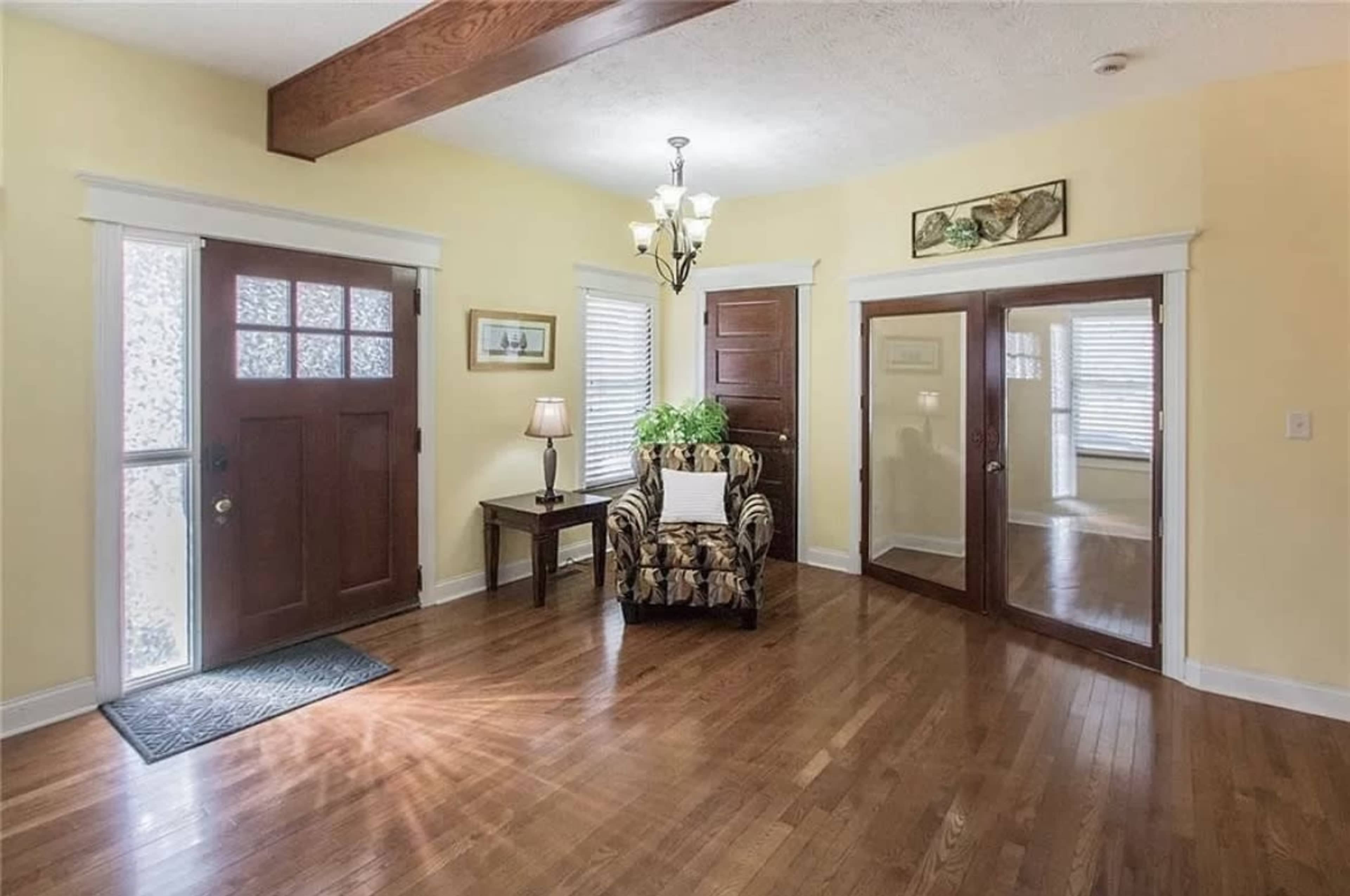 A well-lit entryway with a wooden door, a patterned armchair, and a small table beside a window.
