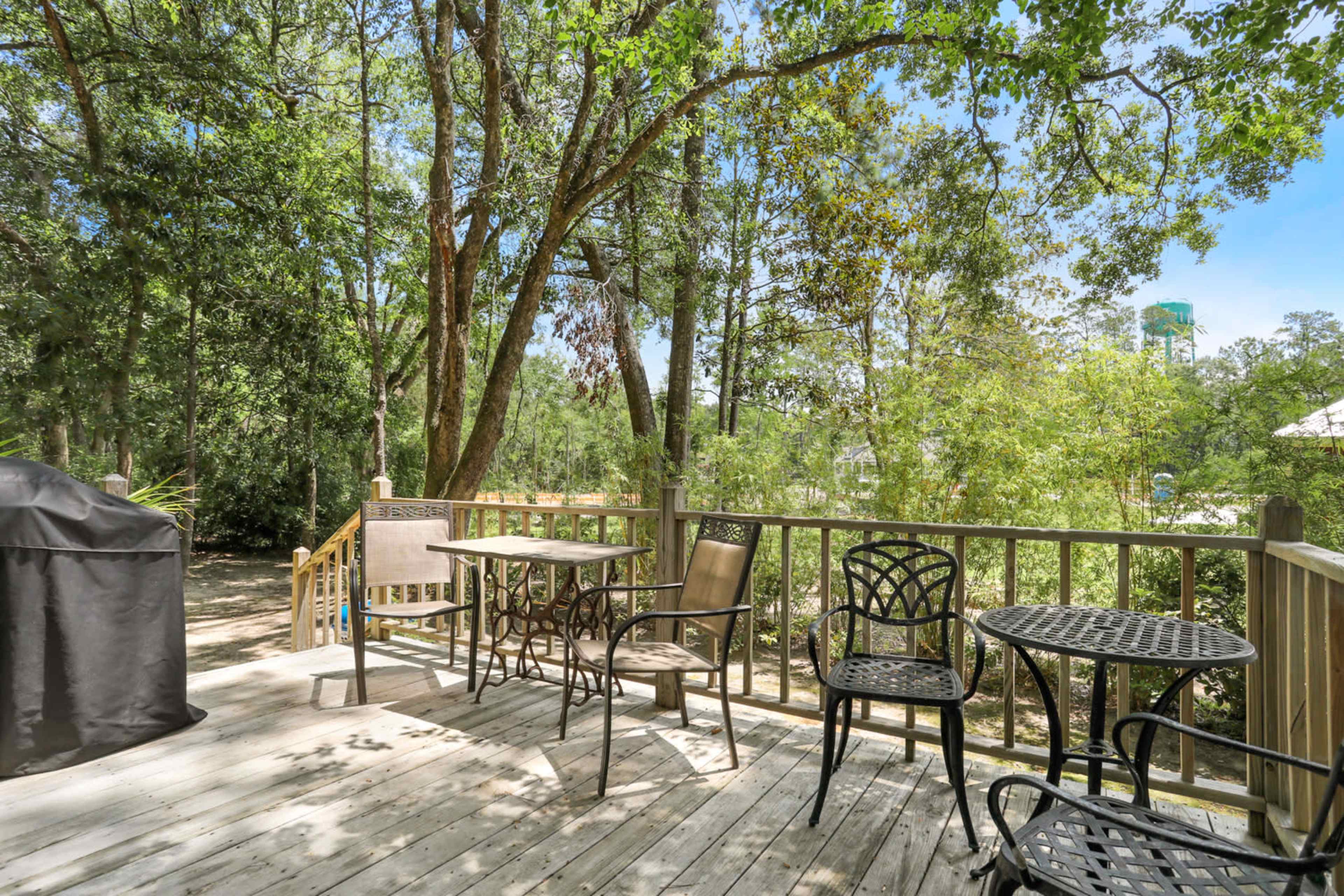 A wooden deck features several metal and wooden chairs and tables surrounded by trees.