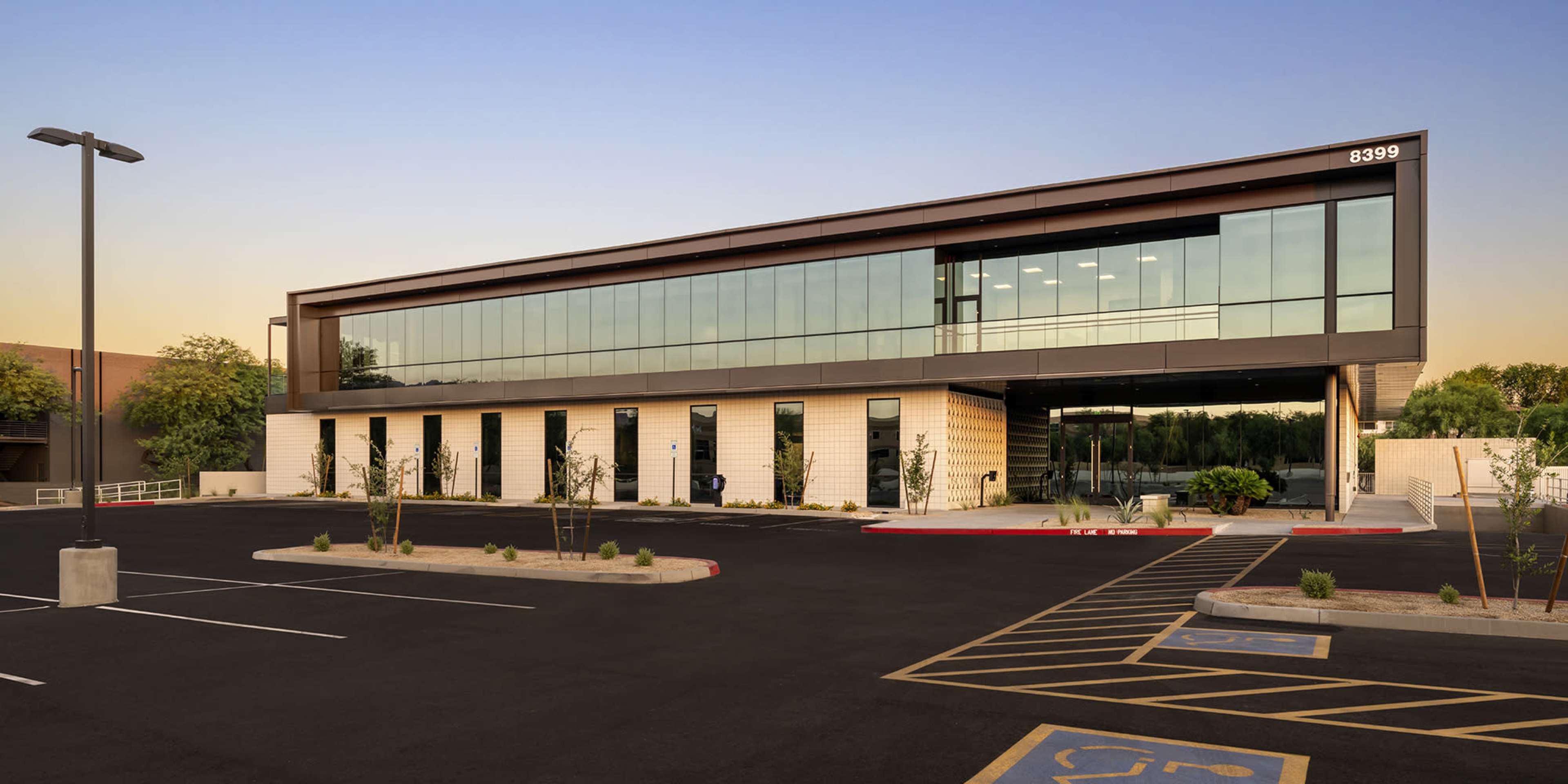 A modern two-story office building with large glass windows and a spacious parking lot is shown in the image.