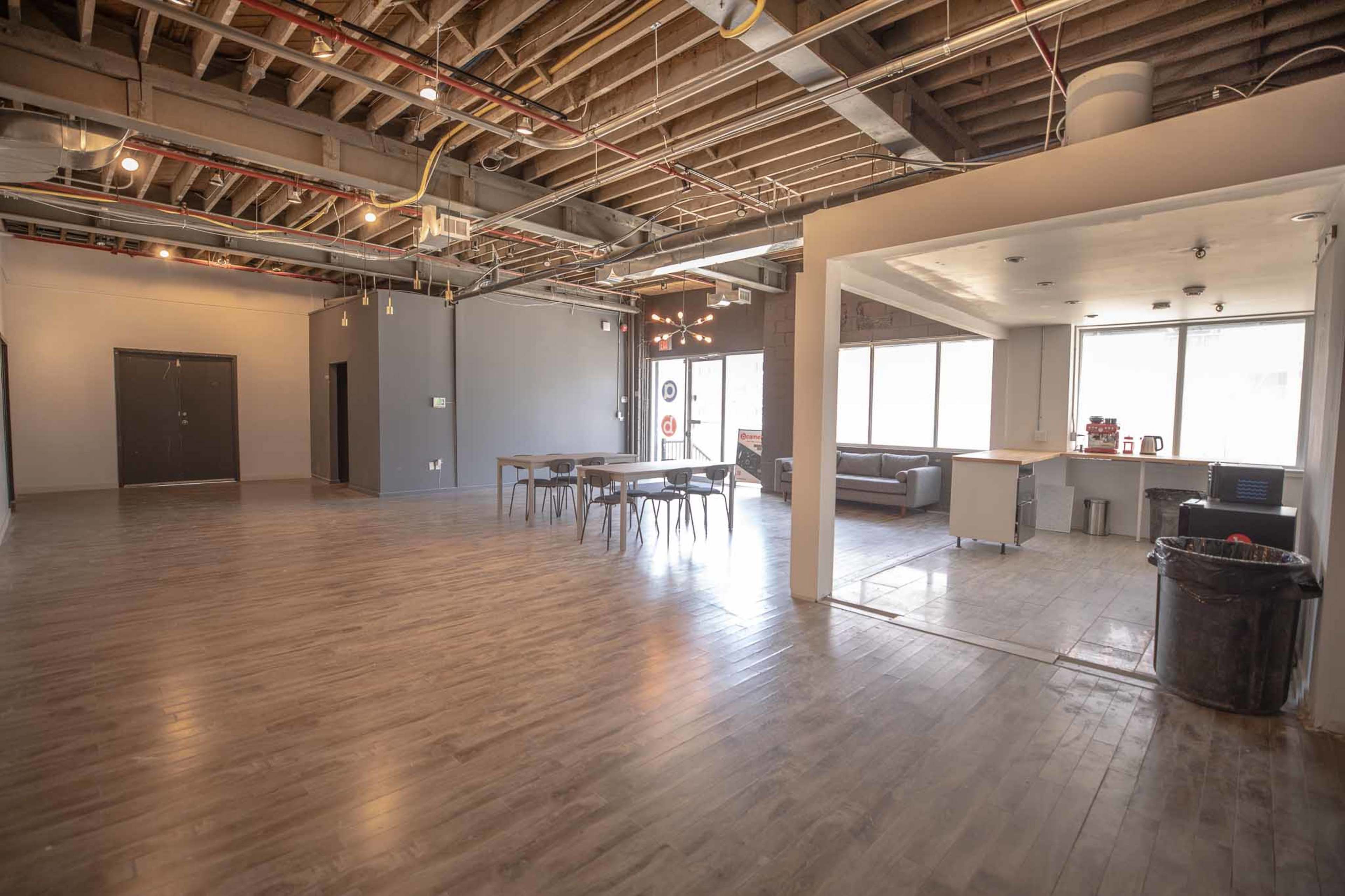 A spacious, unfinished interior features a large open area with wooden flooring, a dining table, and a kitchenette in one corner.