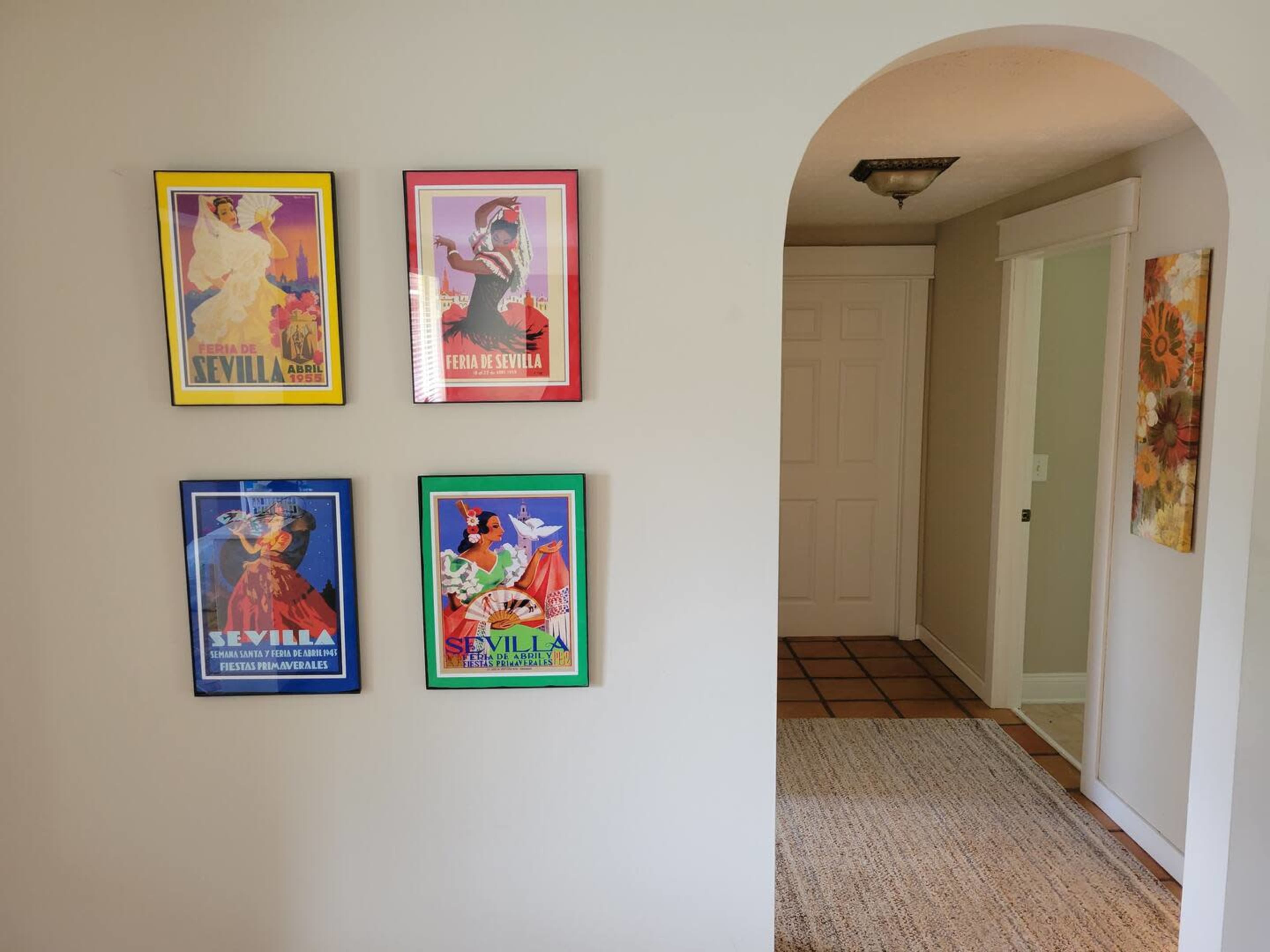 A wall featuring four colorful framed posters related to "Feria de Sevilla," with an arched entrance leading to a hallway on the right.