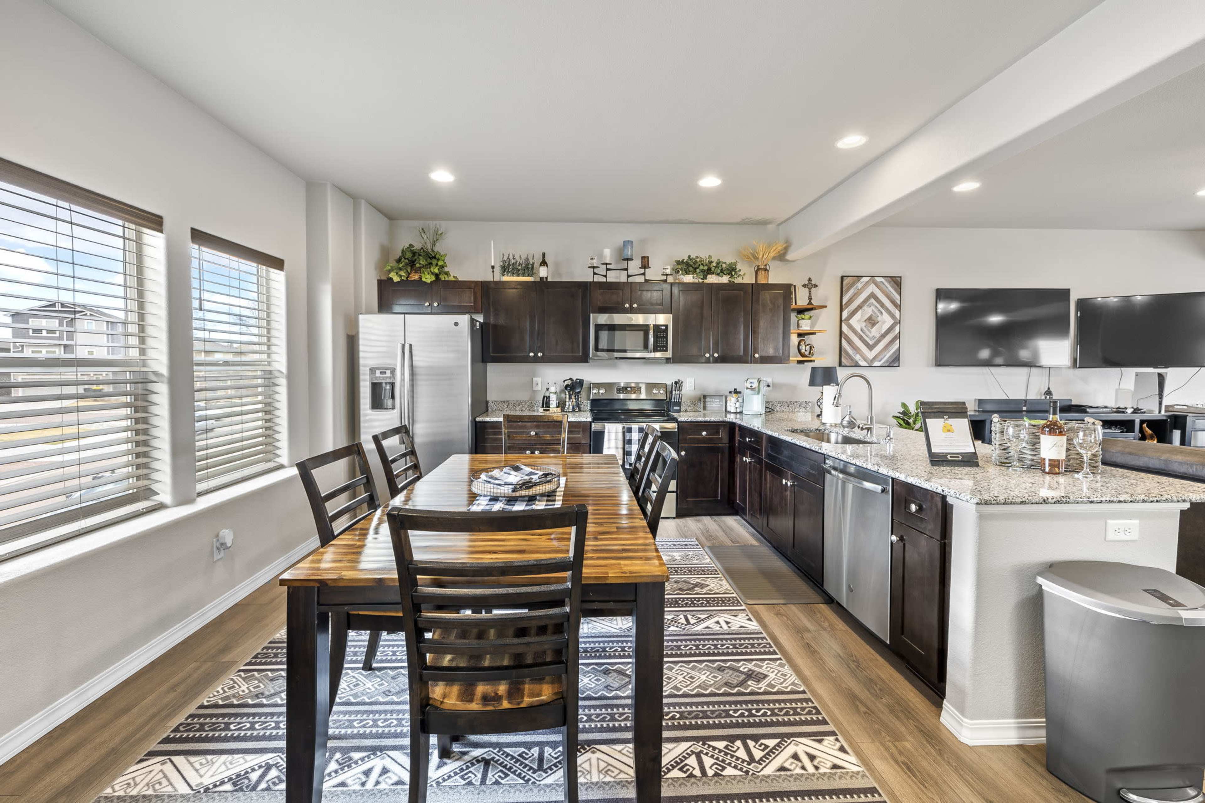 A modern kitchen and dining area with dark wood cabinetry, stainless steel appliances, and a wooden dining table set for meals.