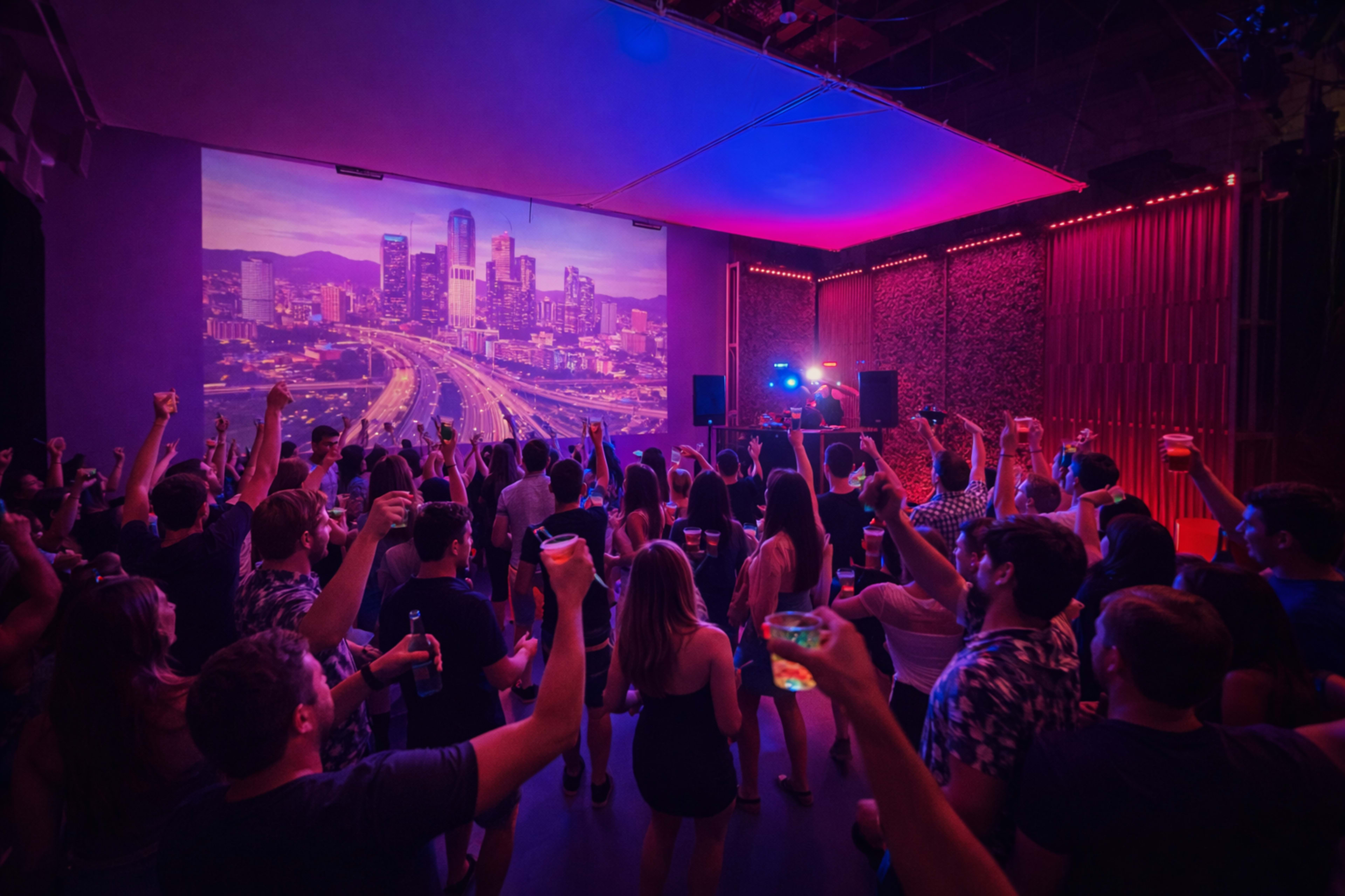 A large group of people raises their drinks while dancing and enjoying a DJ performance in a vibrant venue illuminated by colorful lights.