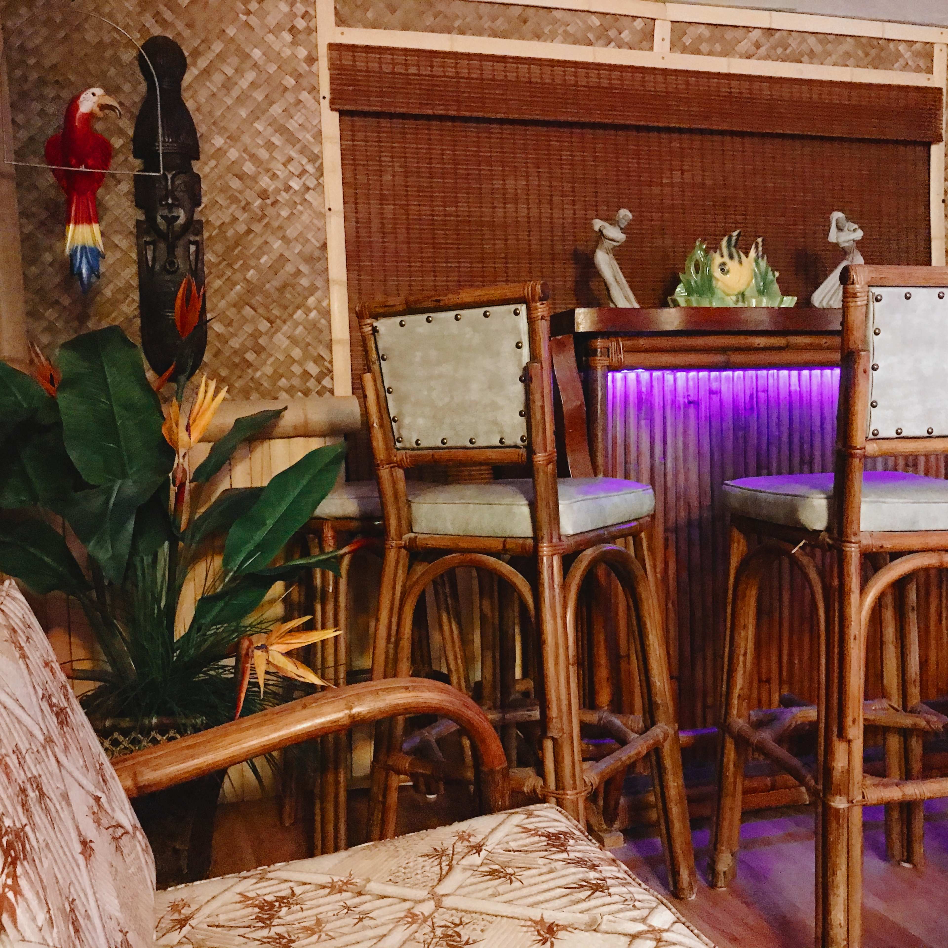 A bamboo bar area features high stools, tropical plants, and decorative elements including a carved figure and a colorful parrot.