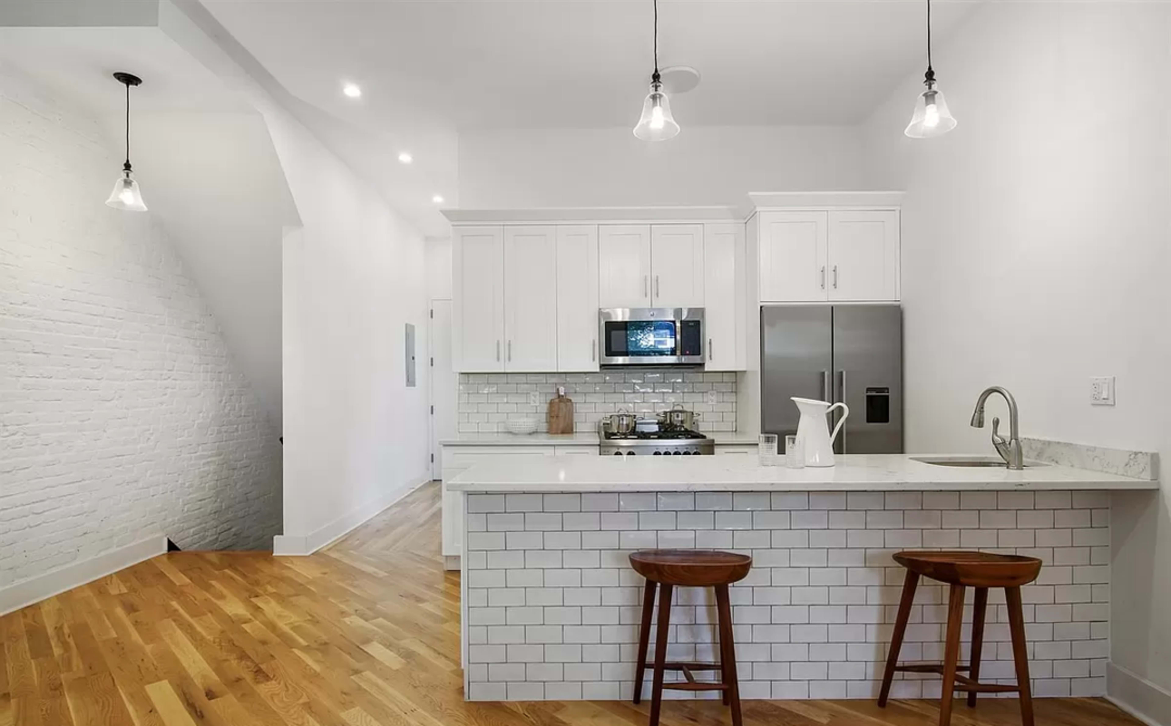 A modern kitchen features white cabinetry, stainless steel appliances, and a marble countertop with two wooden bar stools.