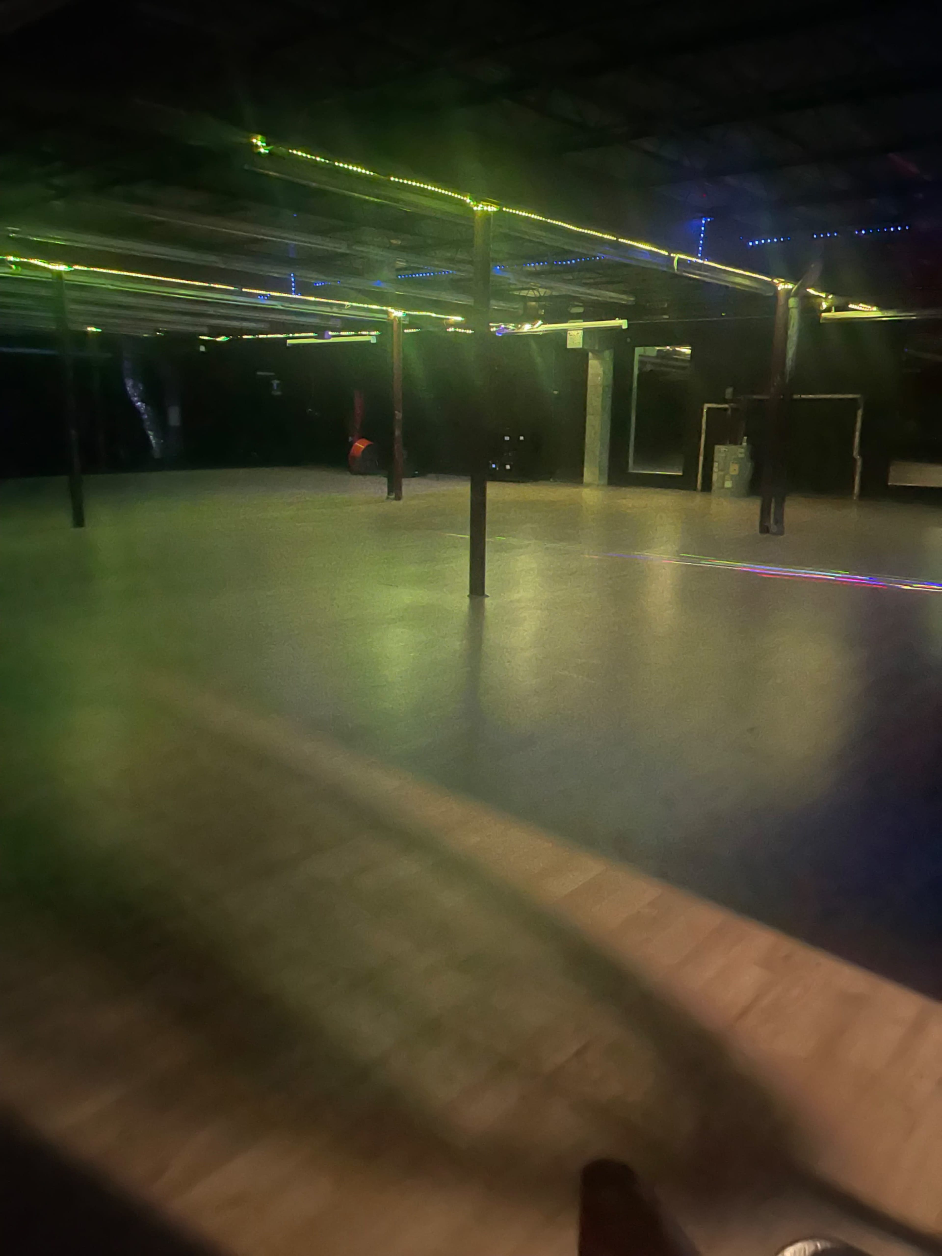 The image shows an indoor space with a wooden floor, illuminated by colorful lights and empty except for a few vertical poles.