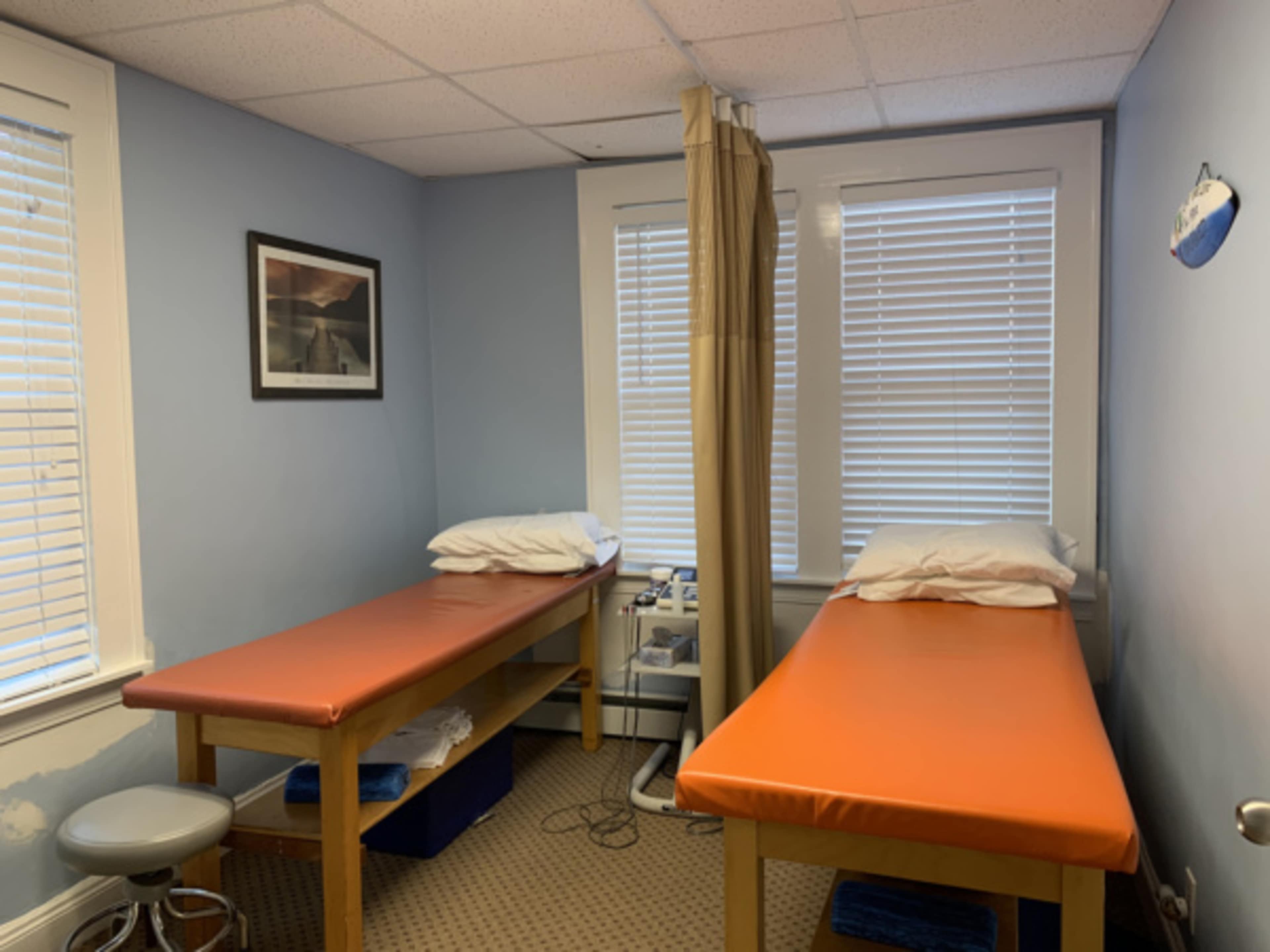 The image shows a small room with two treatment tables, each covered in orange material, and a rollaway privacy curtain between them.