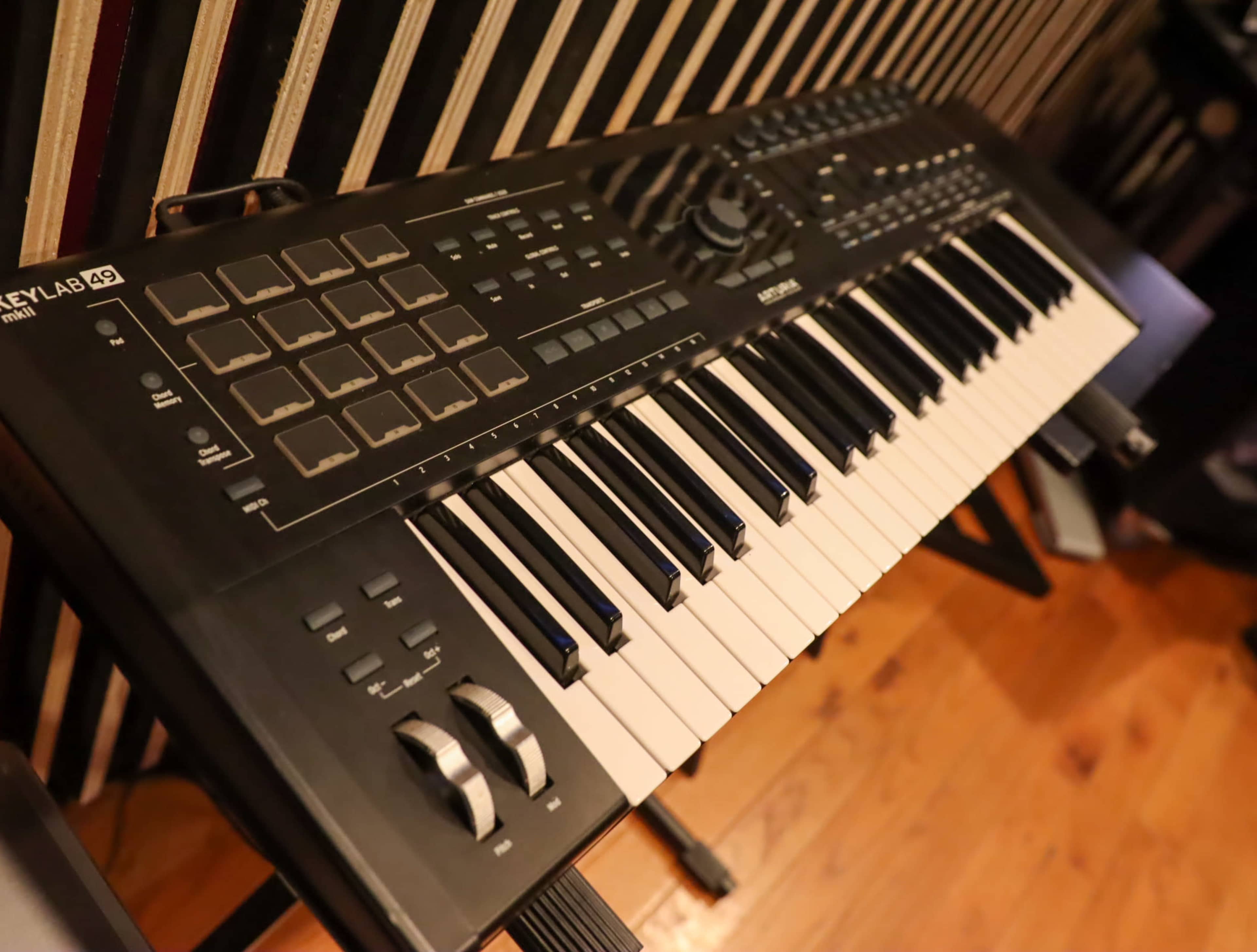 A MIDI keyboard placed on a wooden floor with black-and-white keys and various control buttons.