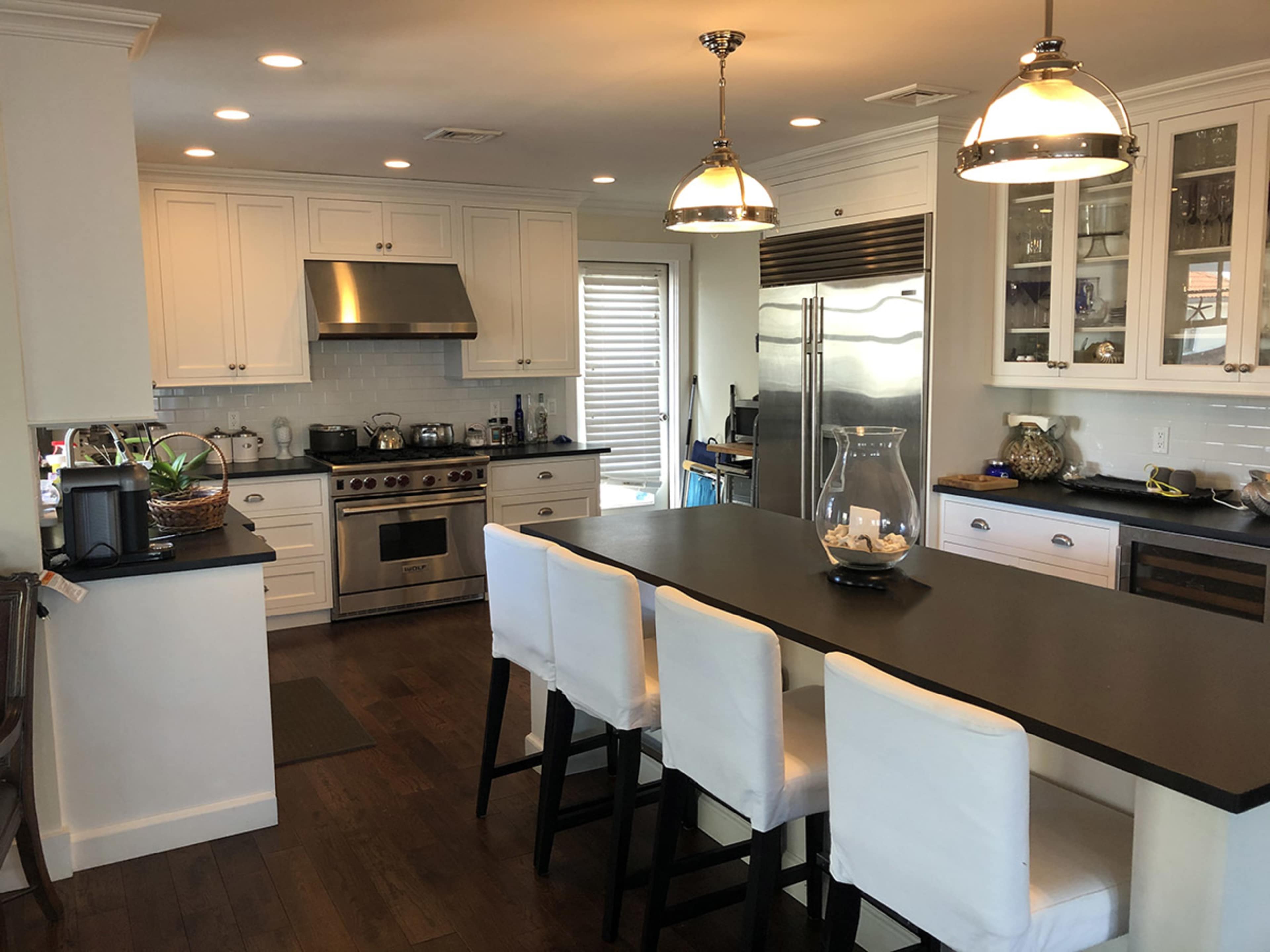 The image shows a modern kitchen with white cabinetry, a stainless steel stove, and a large island with white bar stools.