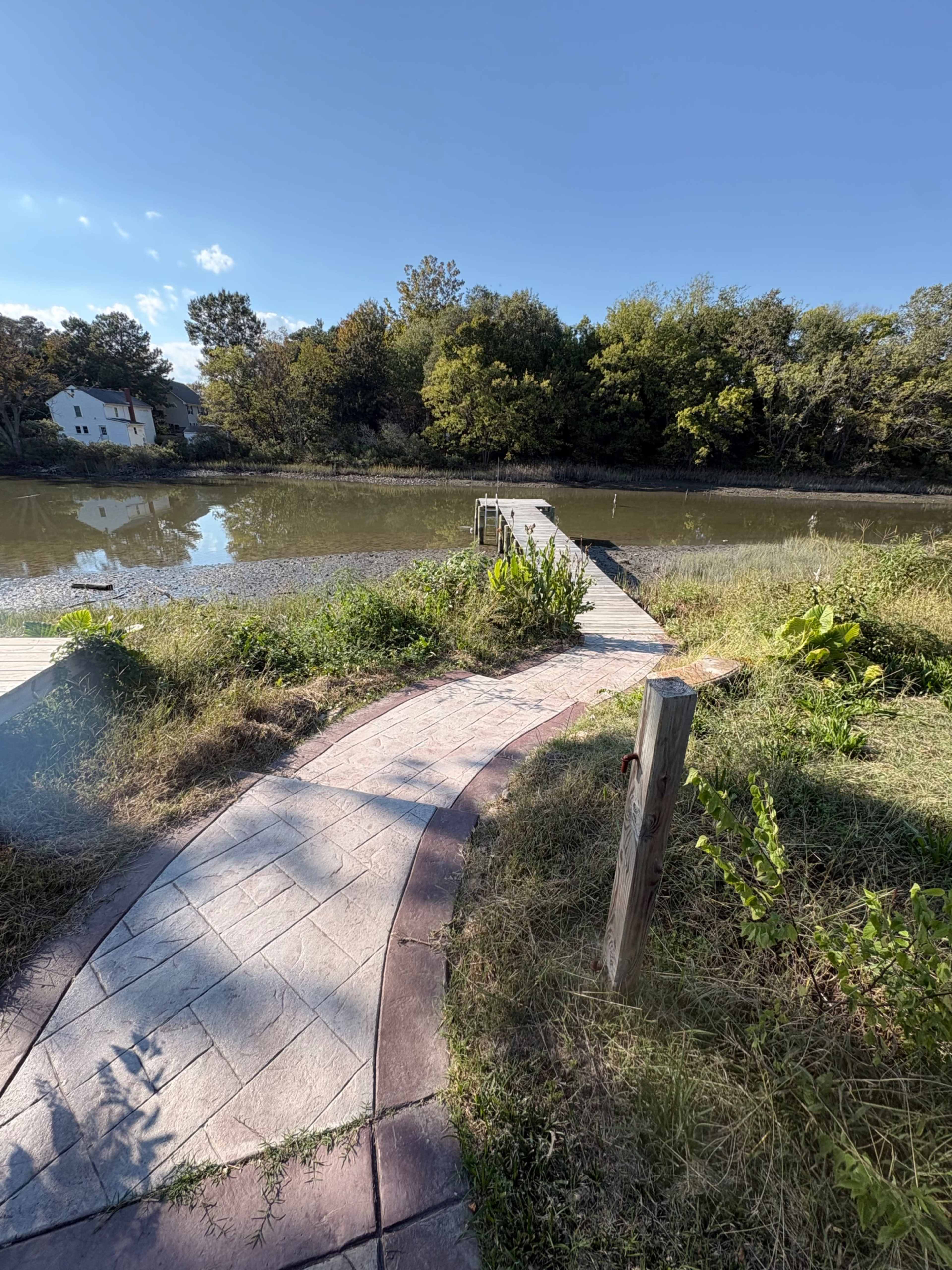 A stone path leads to a wooden dock extending into a calm river surrounded by lush greenery.