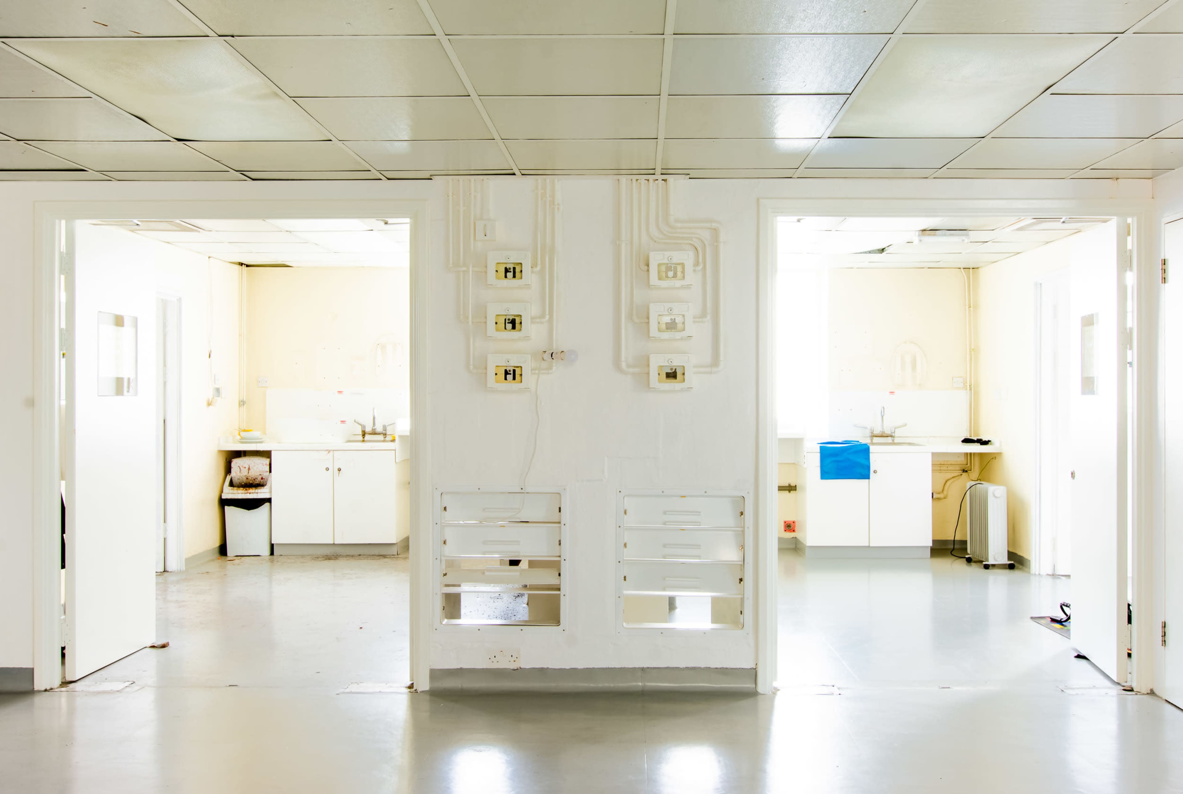 A bright, empty corridor with two open doorways leading to adjacent rooms that contain sink areas and cabinets.