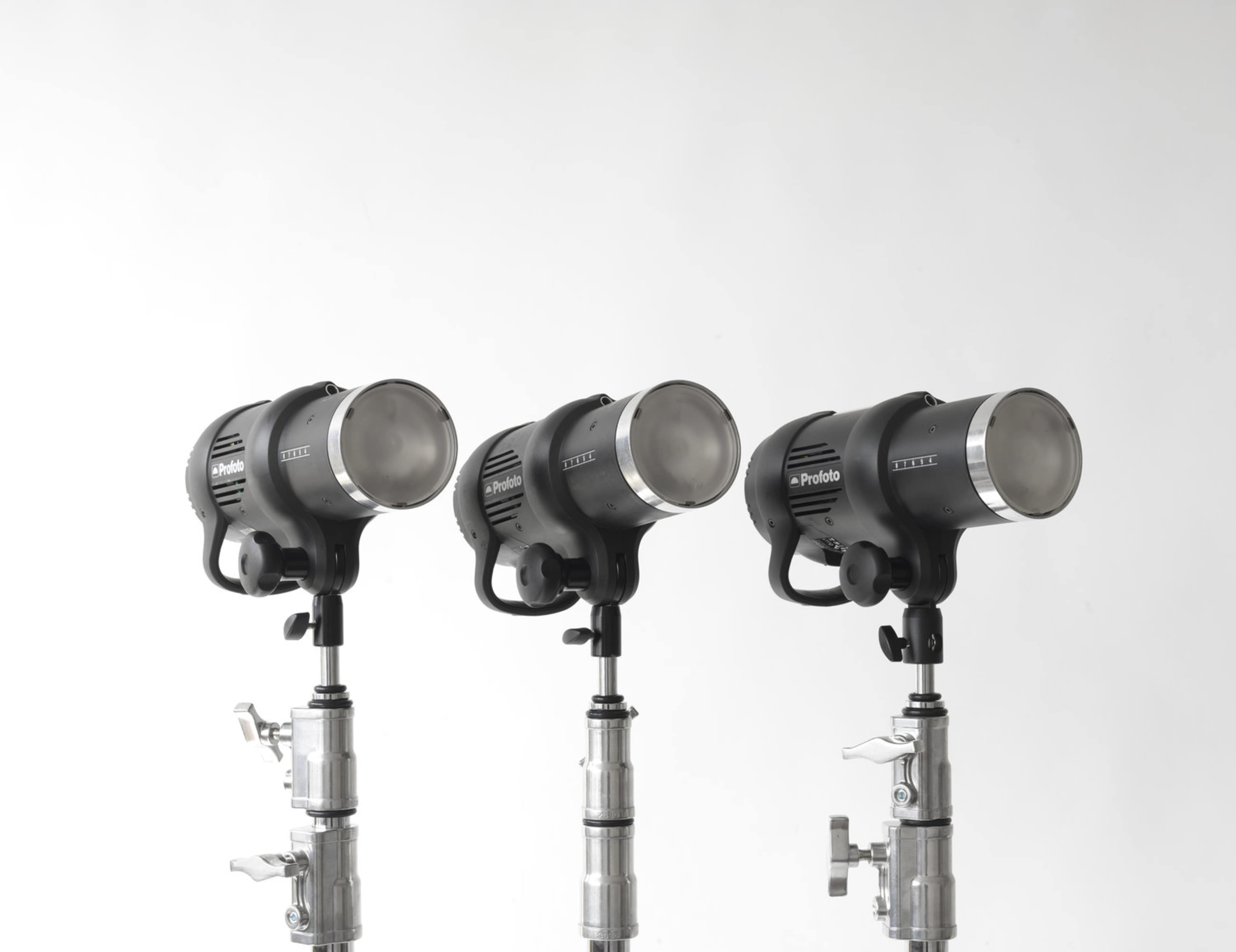 Three studio flash lights mounted on stands against a plain white background.