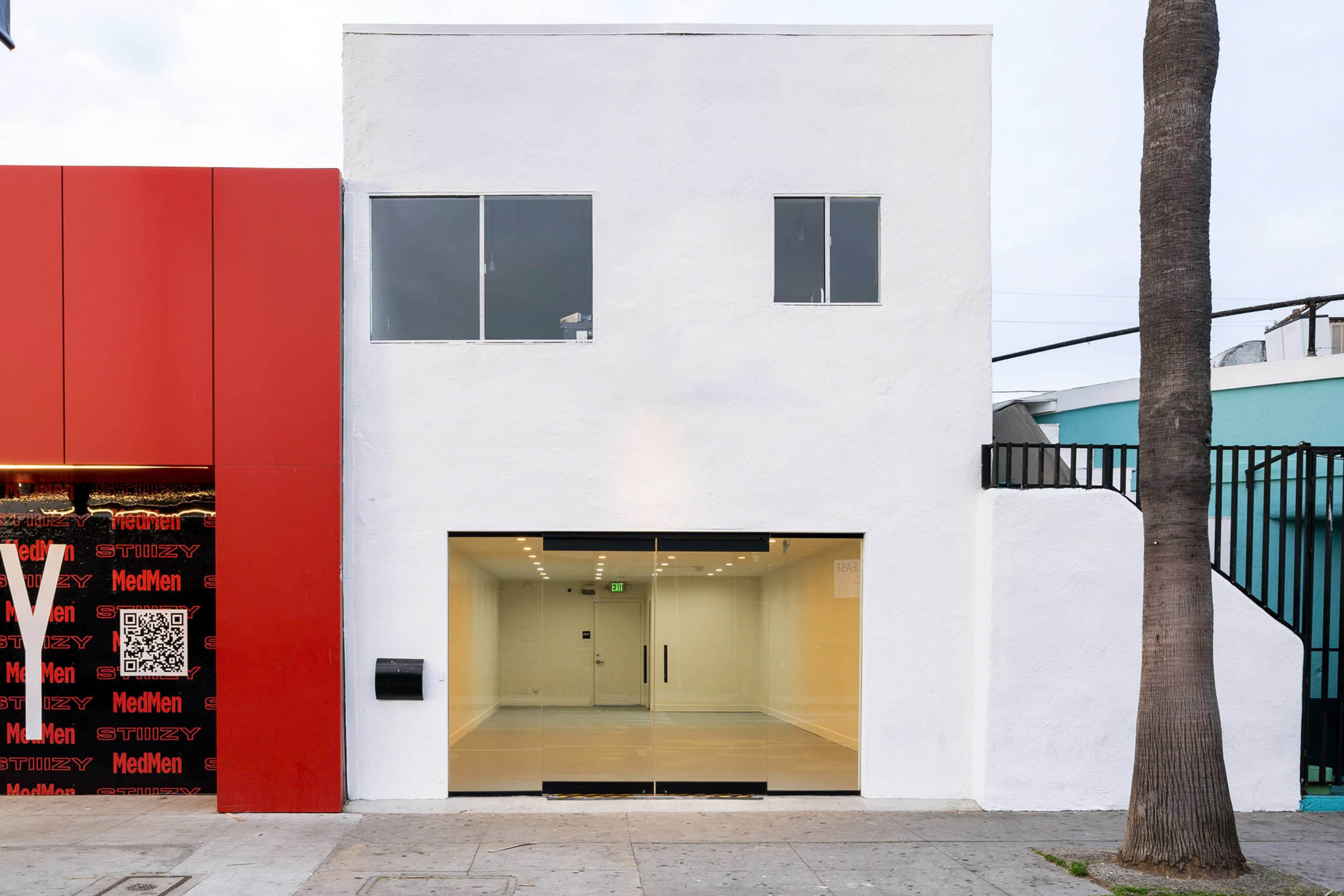 The image shows a modern white building with large windows and a glass entrance, situated next to a red structure.