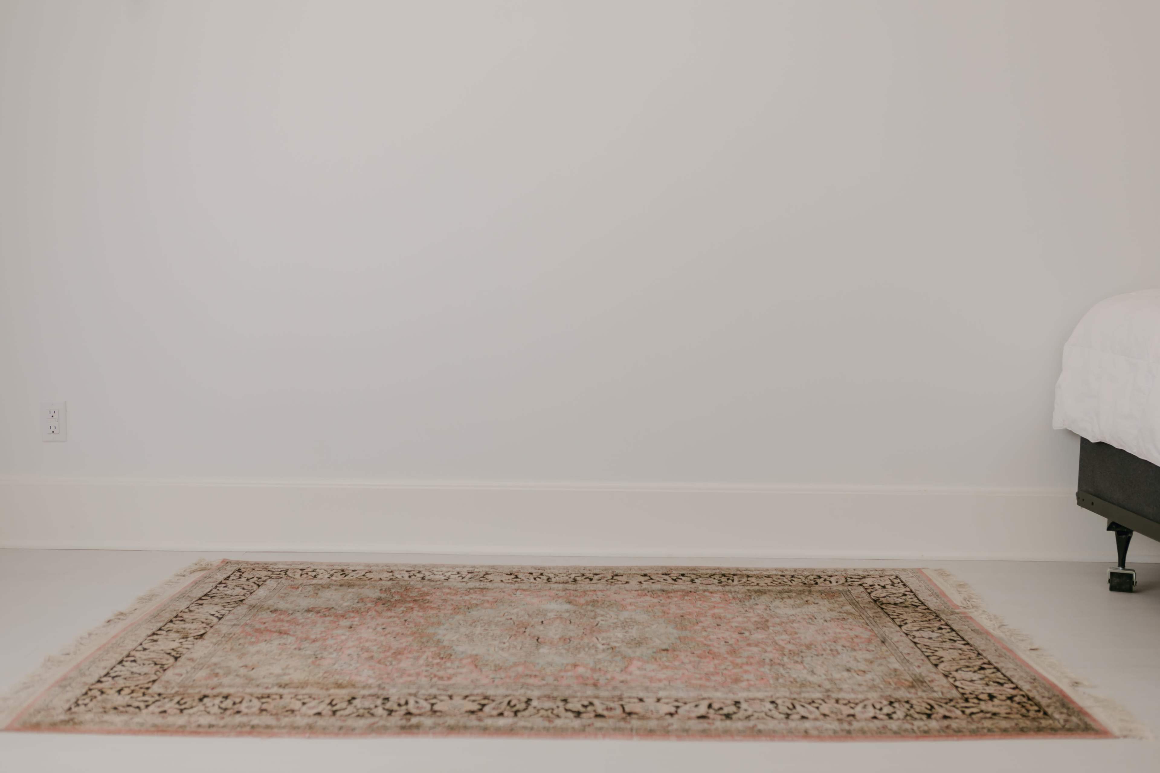 A vintage area rug lies on a smooth, light-colored floor in a minimally decorated room.