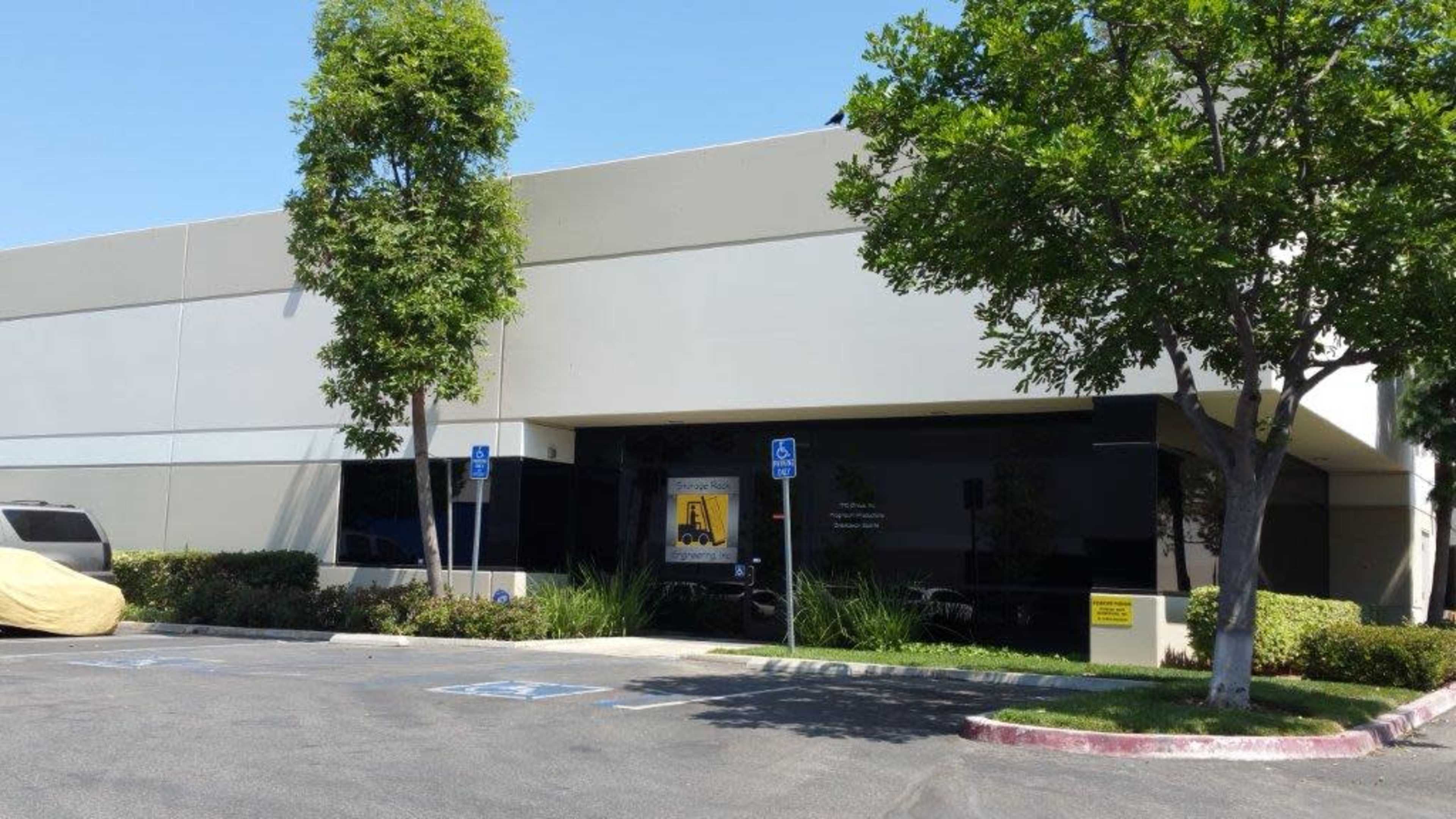 The exterior of a commercial building with large windows and landscaped greenery in a parking lot.