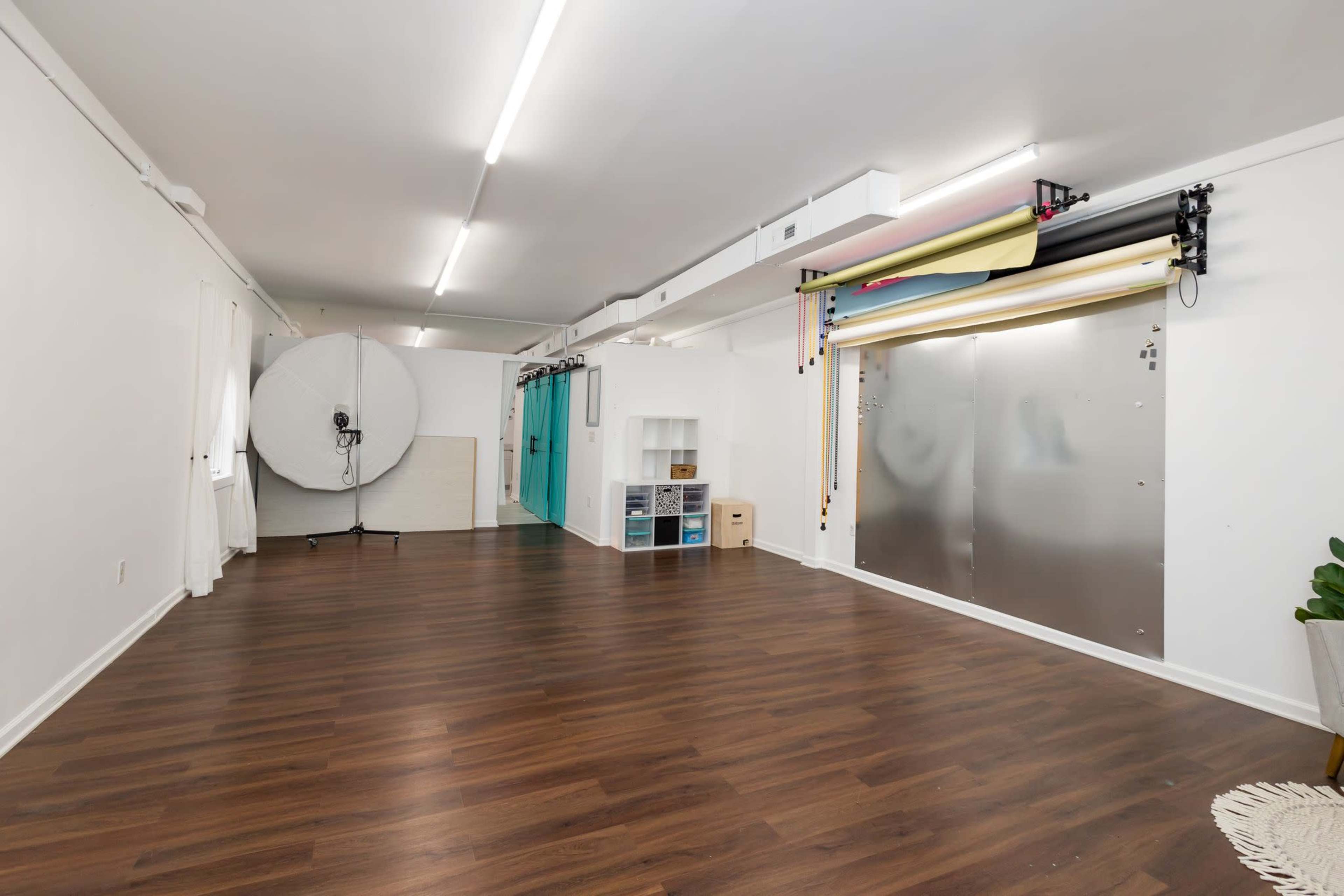 A spacious room with wooden flooring, a round backdrop, and a setup for various colored backgrounds along one wall.