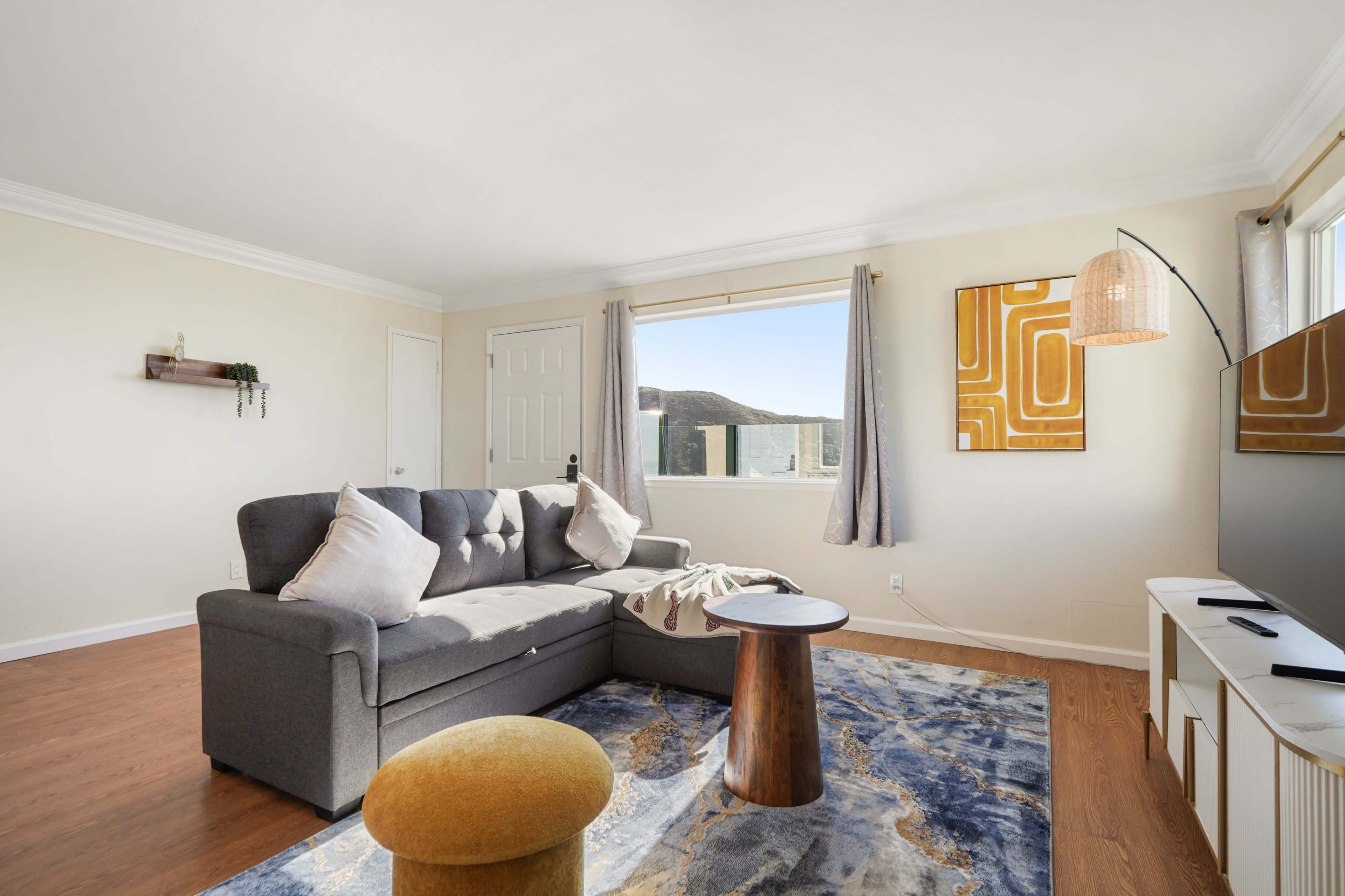 A modern living room features a gray sofa, a wooden coffee table, and a large area rug, with a window providing a view of the outdoors.