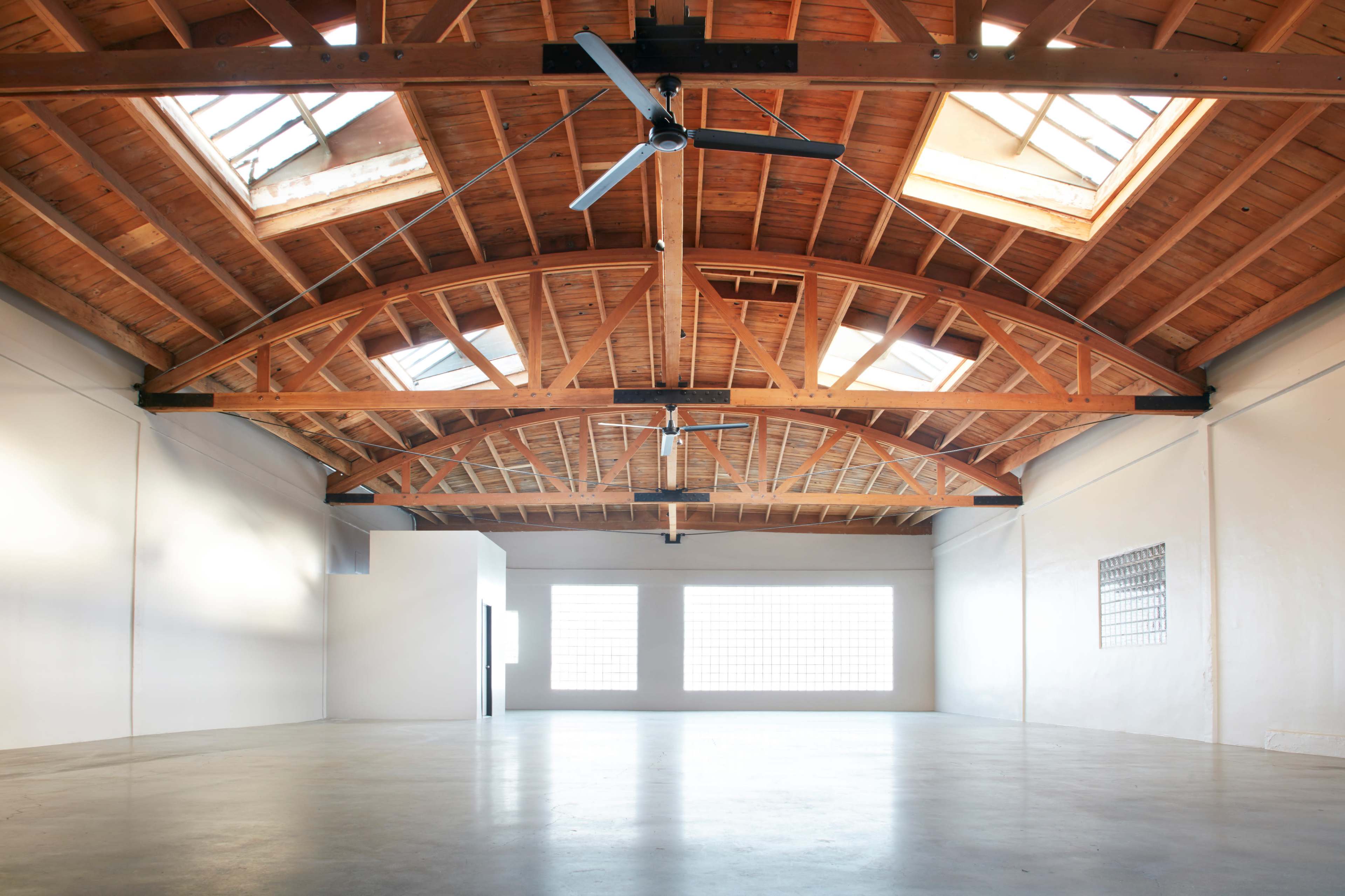 A spacious, empty room with a high wooden ceiling and large windows allowing natural light.