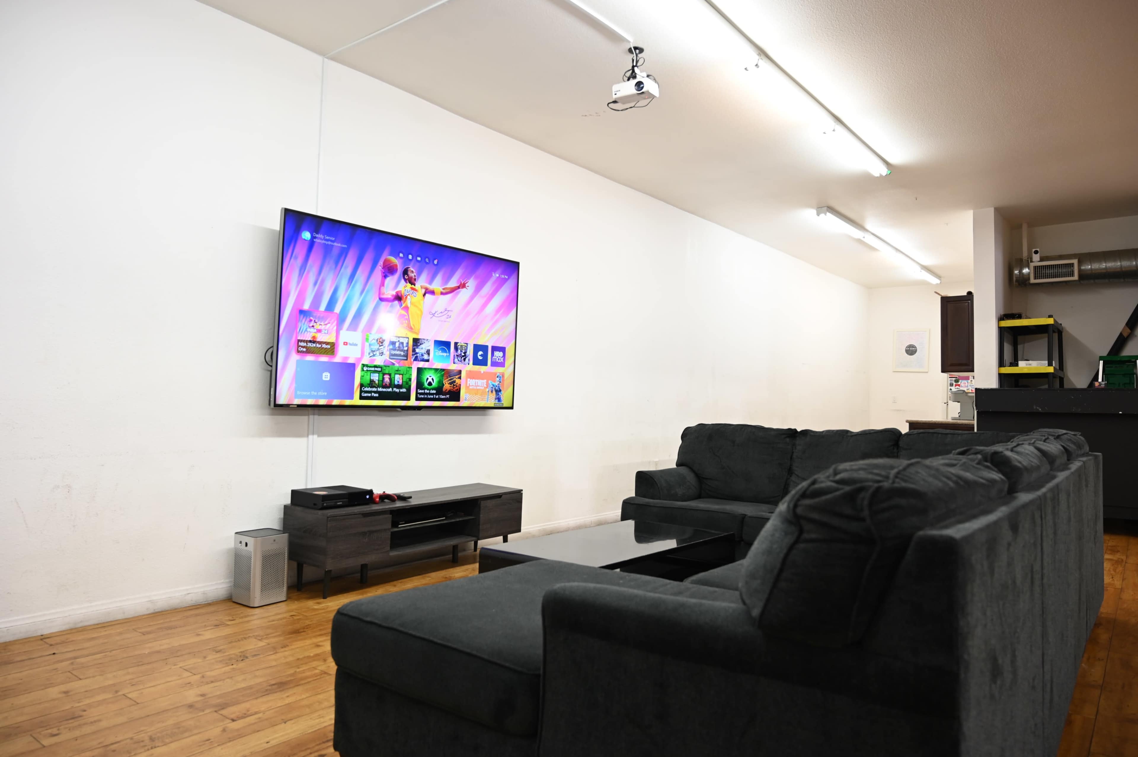A modern living room features a large wall-mounted television displaying a colorful interface, with a dark couch set and wooden flooring.
