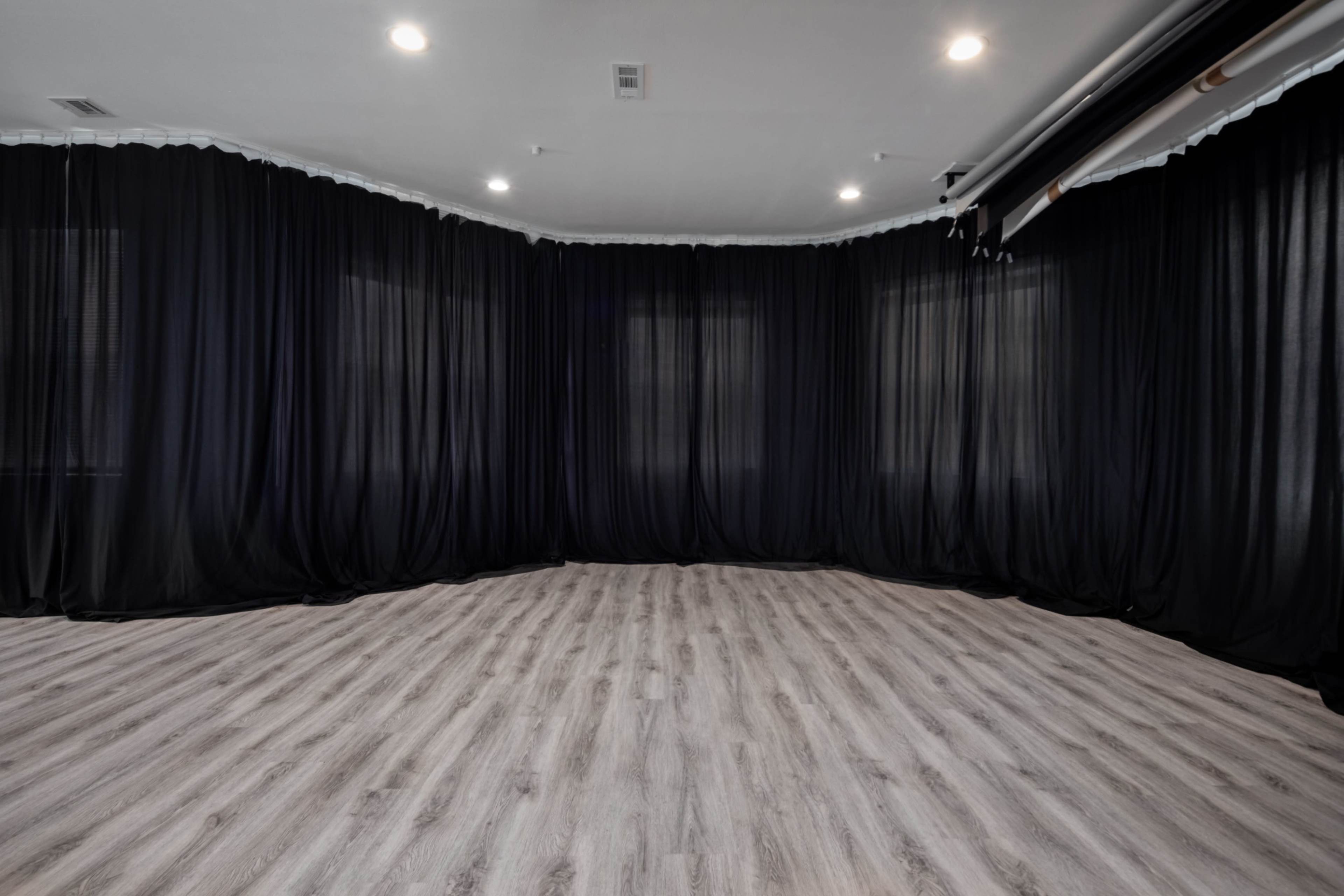 The image shows a spacious room with black drapes lining the walls and a wooden floor.