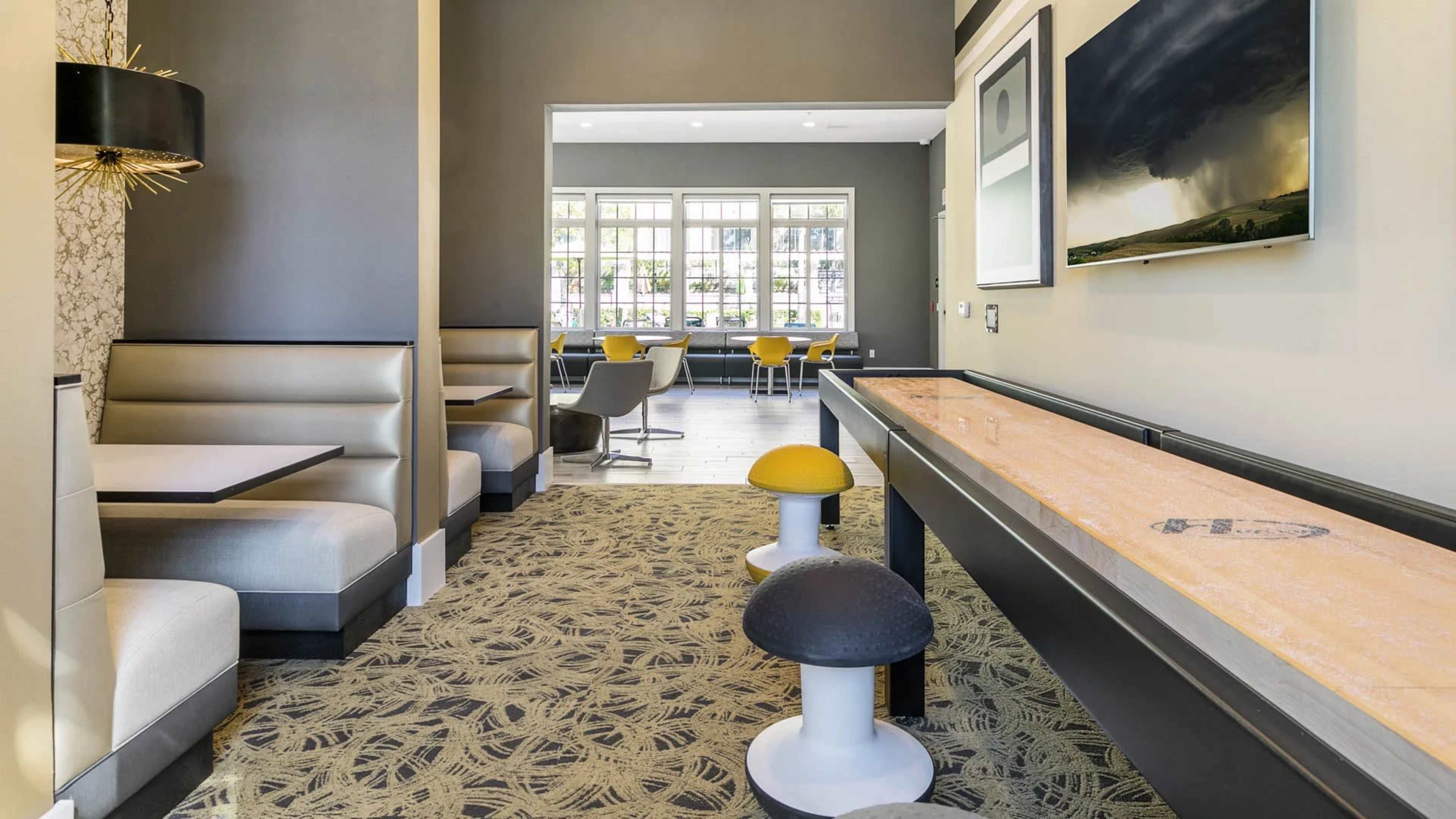 A modern lounge area with cozy seating booths, a long table, and natural light coming through large windows.