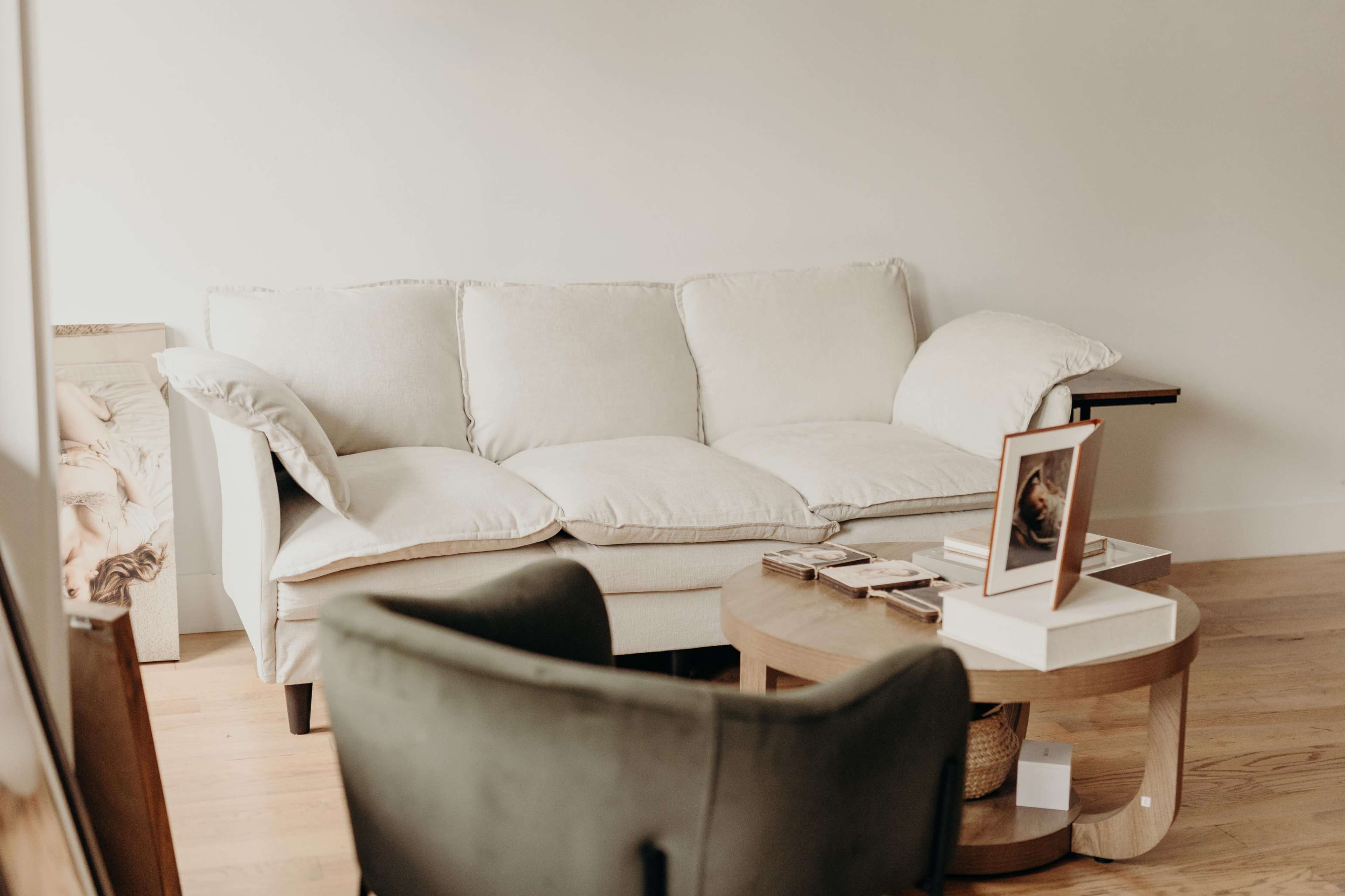 A light-colored sofa sits against a wall, accompanied by a round coffee table that holds a framed photo and a few books.