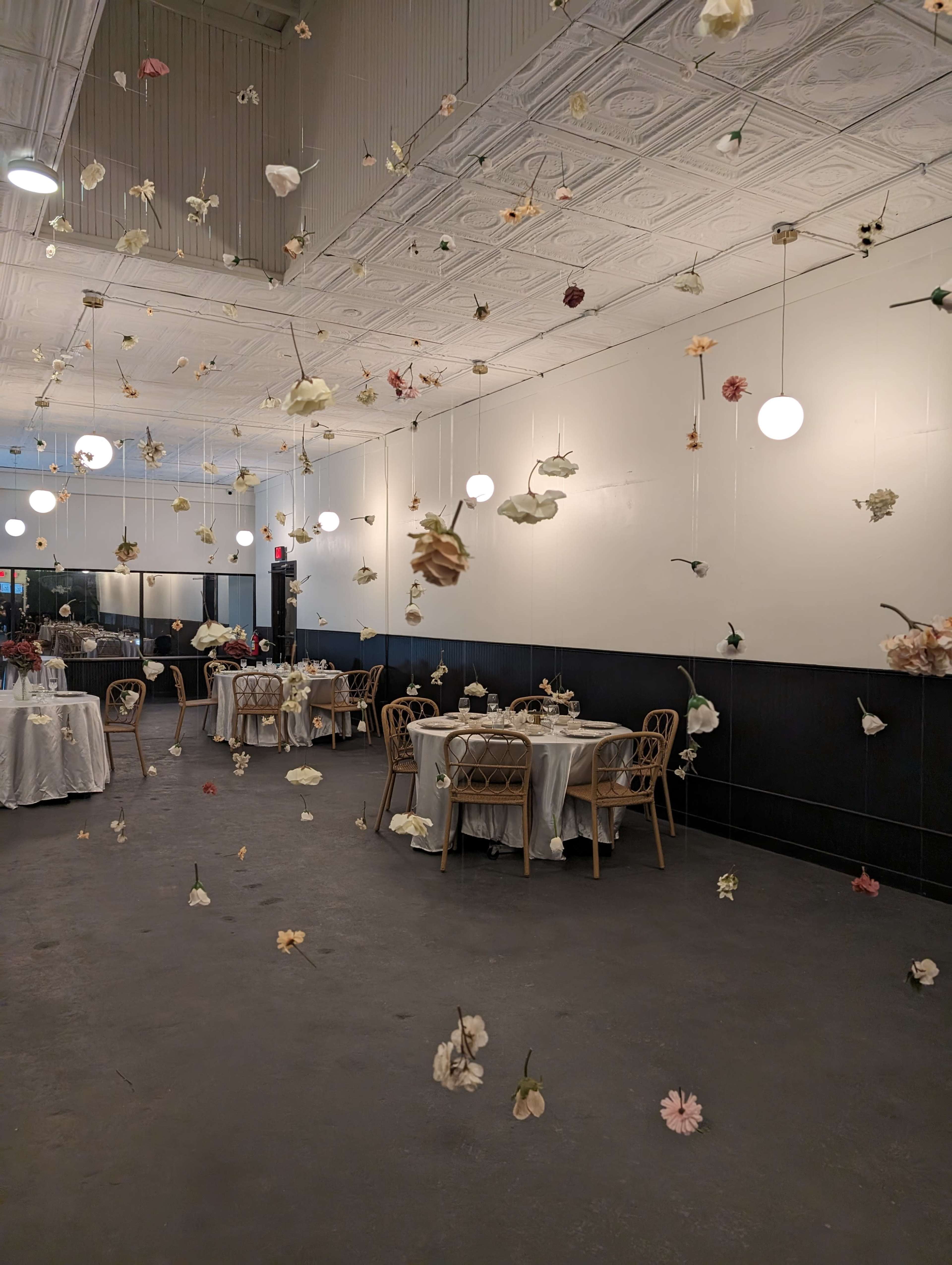 A dining space features tables with white tablecloths surrounded by hanging dried flowers from the ceiling.