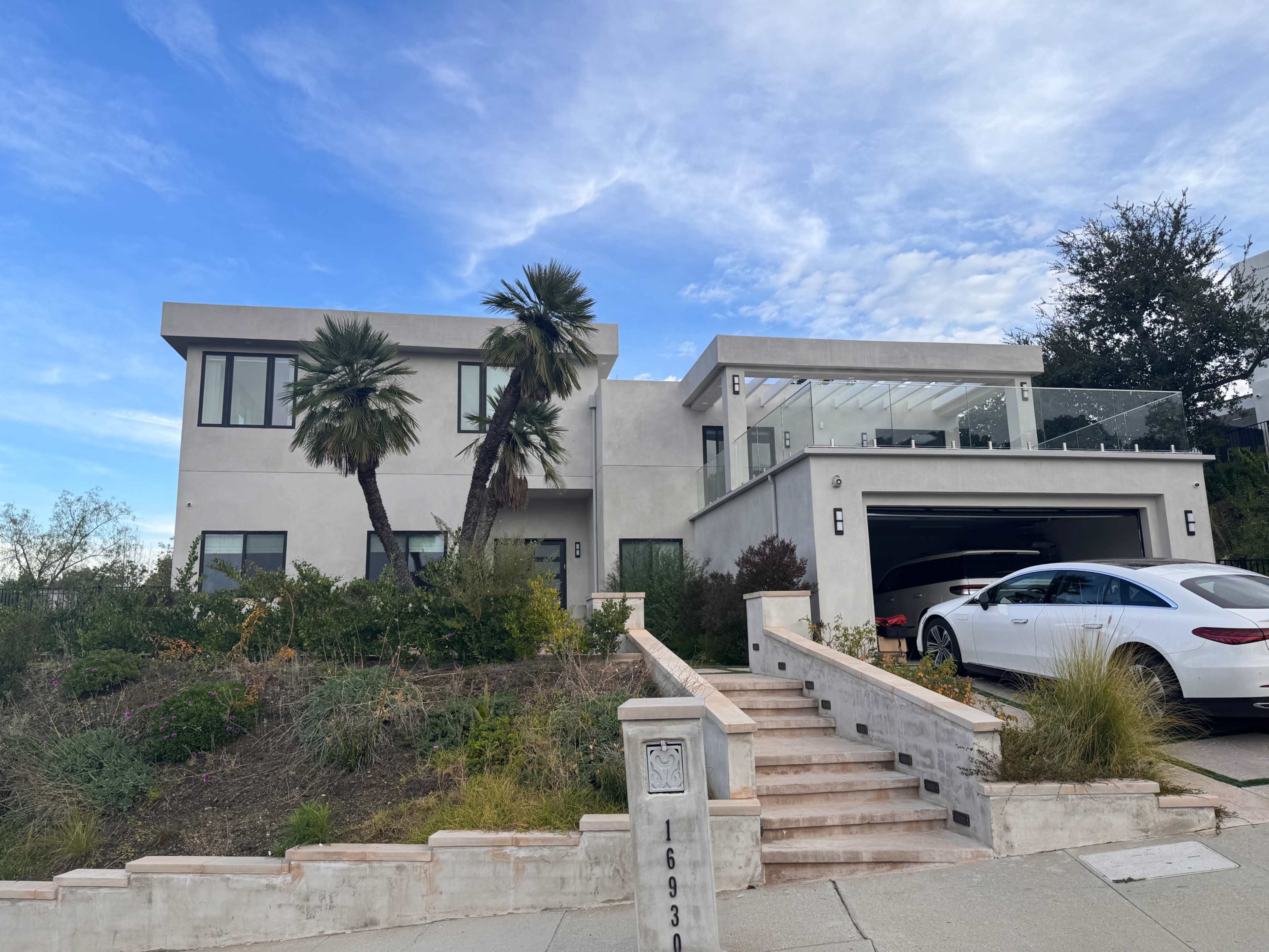 A modern two-story house with palm trees in the front yard and a driveway leading to a garage.