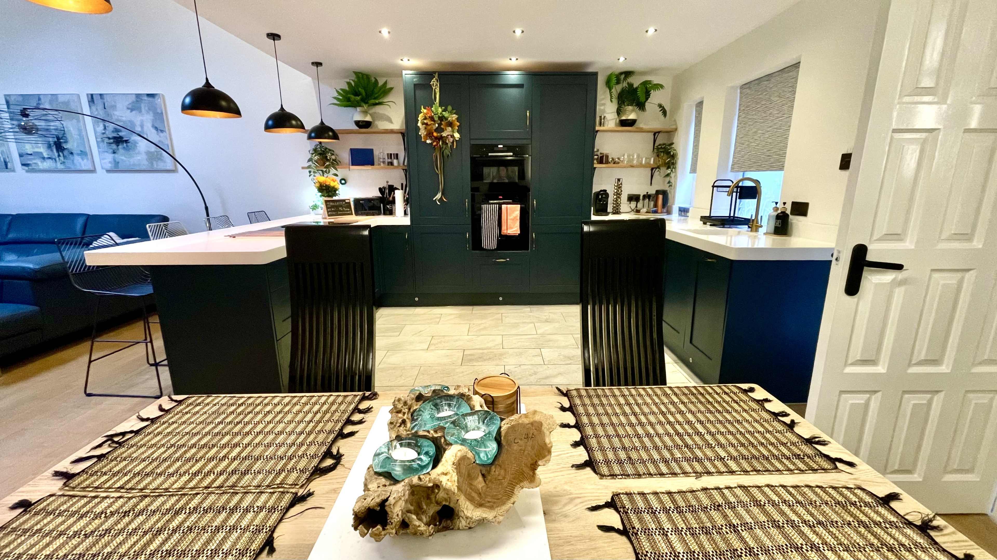 A modern kitchen features dark cabinetry, white countertops, and a wooden dining table set with decorative placemats and a centerpiece.
