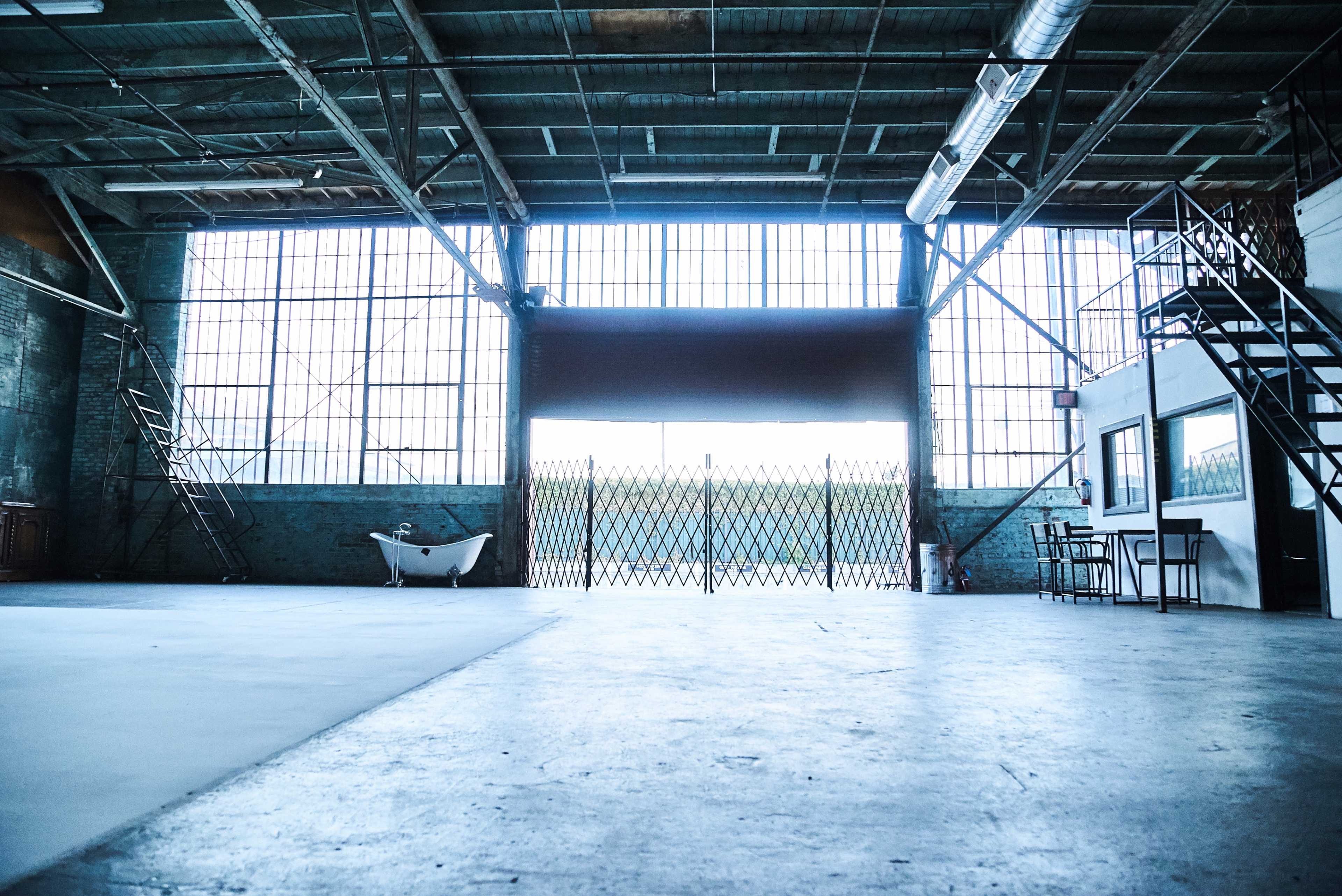 A spacious industrial-style interior with large windows, a bathtub, and a gated entrance.
