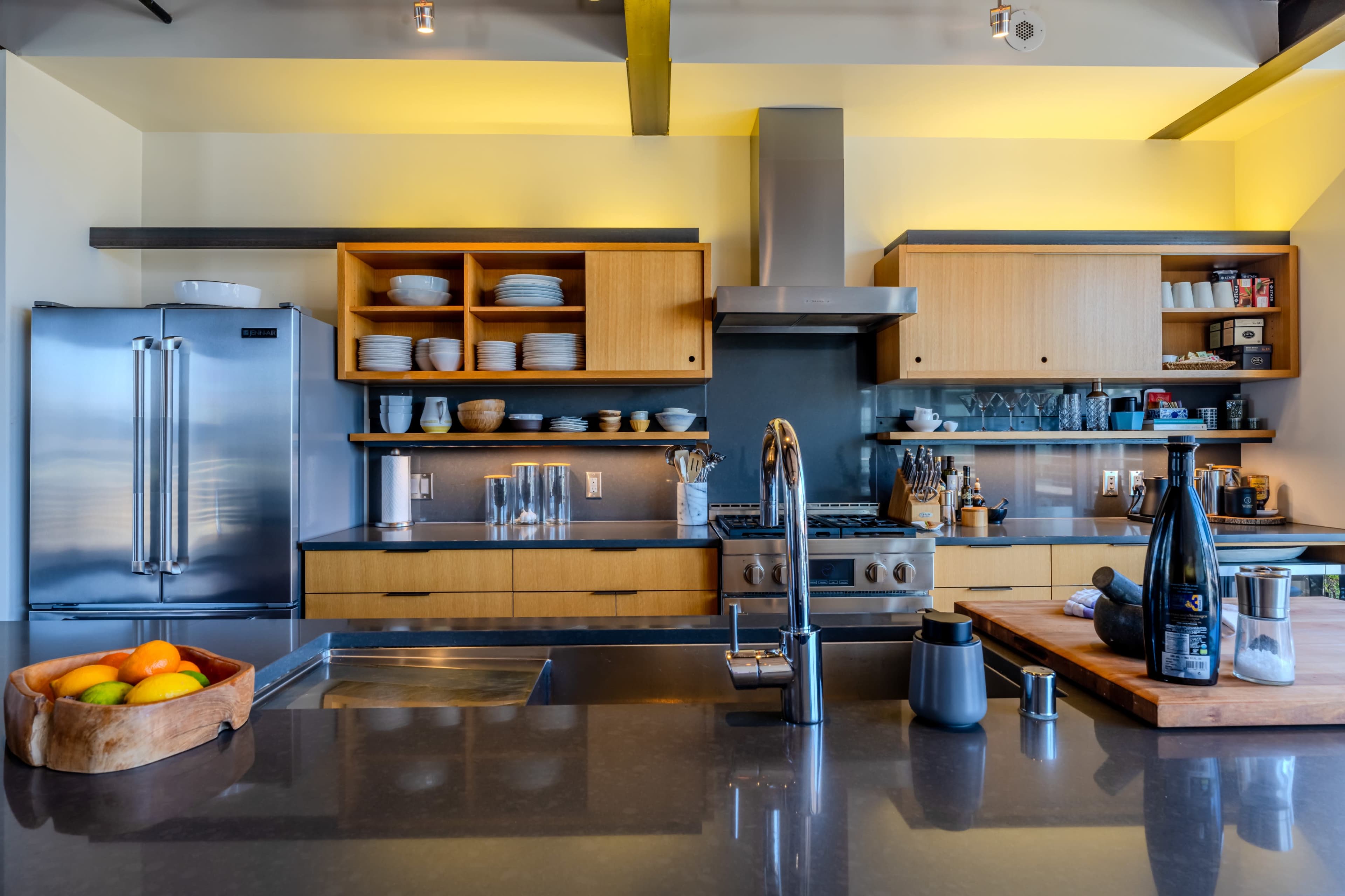 A modern kitchen features stainless steel appliances, wooden cabinetry, and a central island with a bowl of fruit.