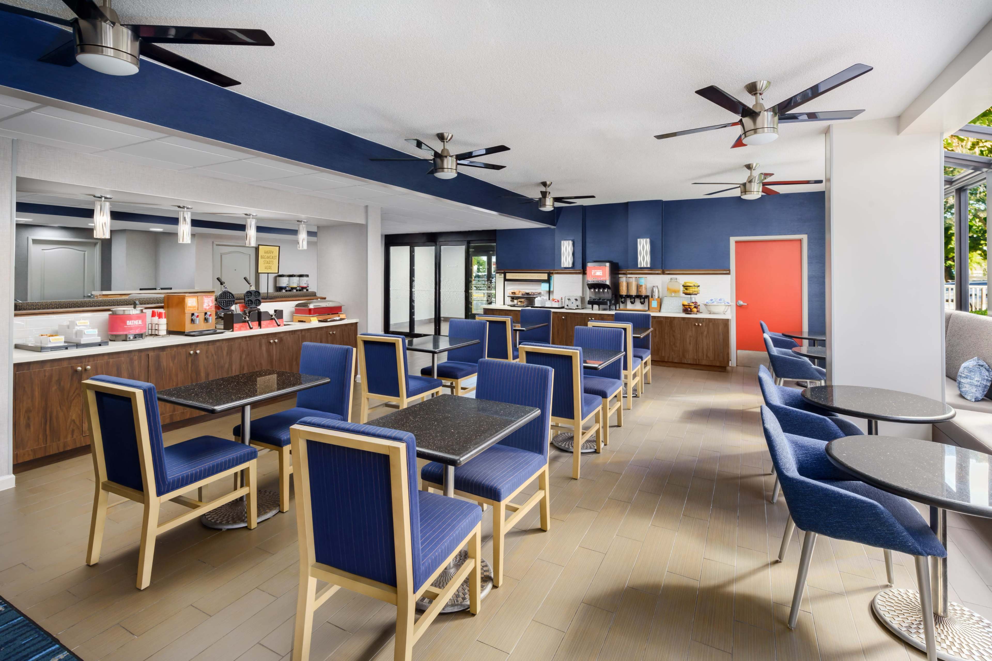 The image shows a modern dining area with blue walls, several tables and chairs, and an open buffet counter.