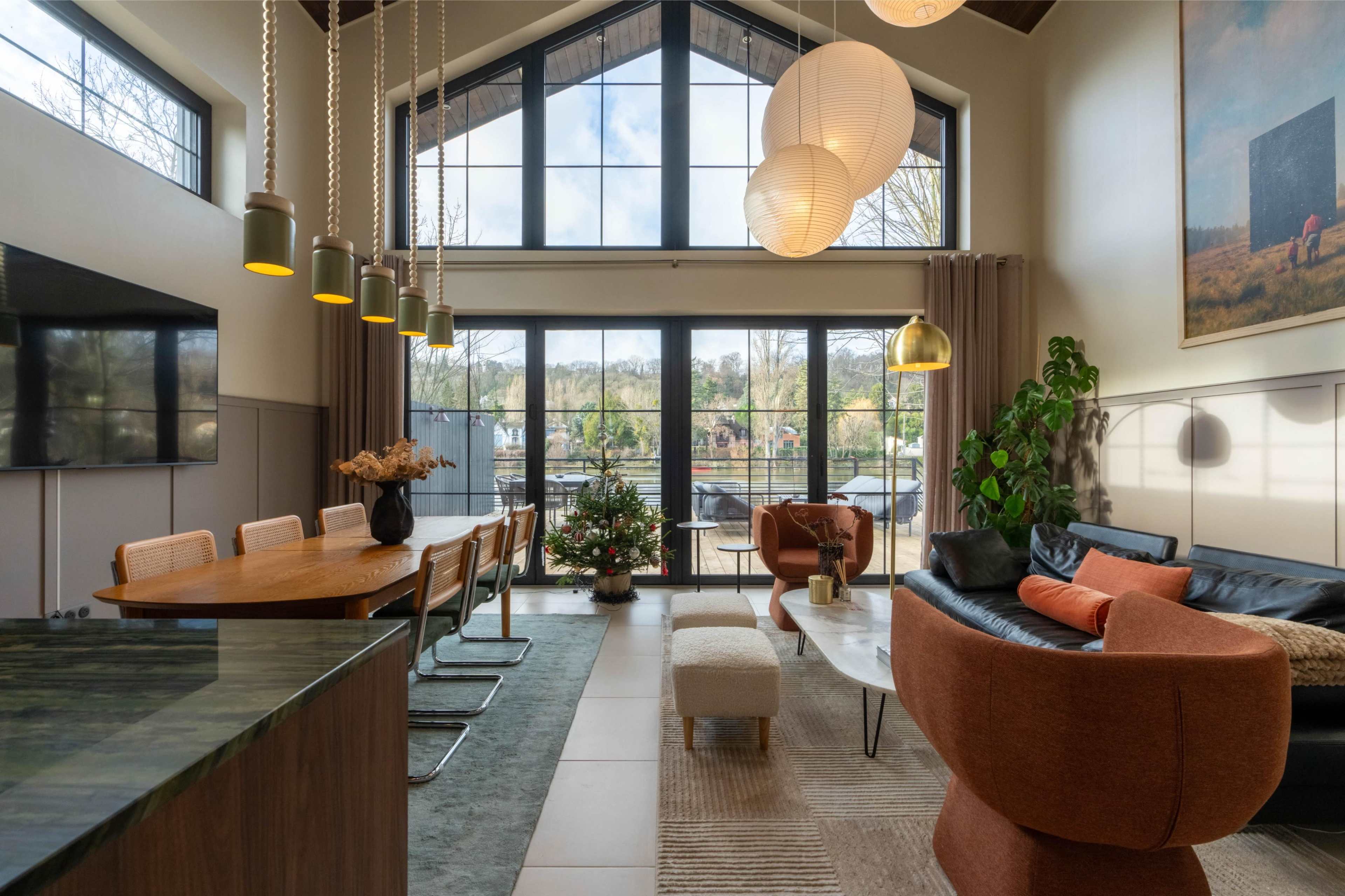 The image shows a modern living space with a large window view of a patio, featuring a dining table, comfortable seating, and decorative plants.