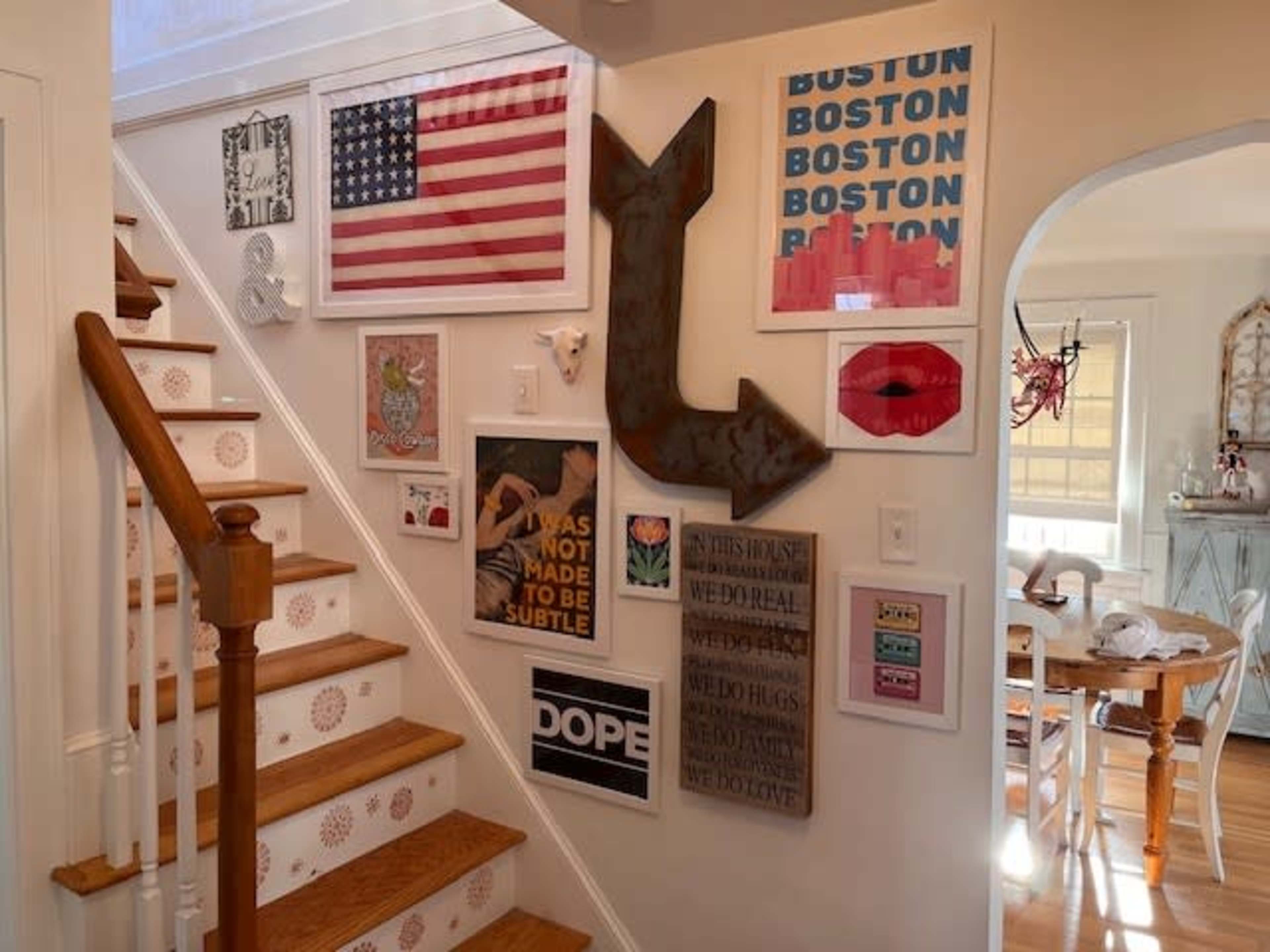 The image features a staircase with a variety of framed artwork and decor displayed on the wall, including a flag, various prints, and an anchor-shaped piece.