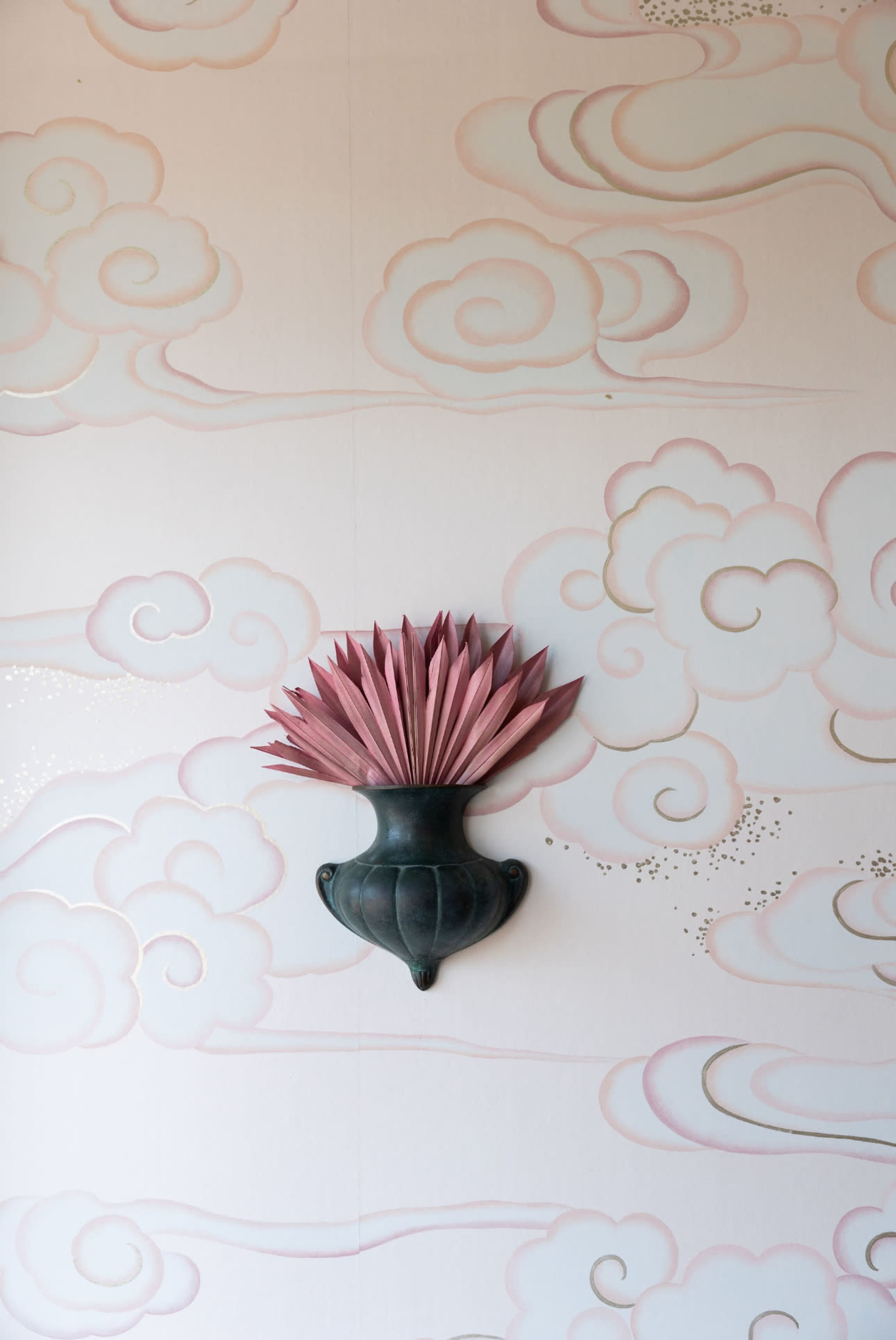 A decorative wall featuring a pink and white cloud pattern, with a dark vase holding pink leaves in the center.