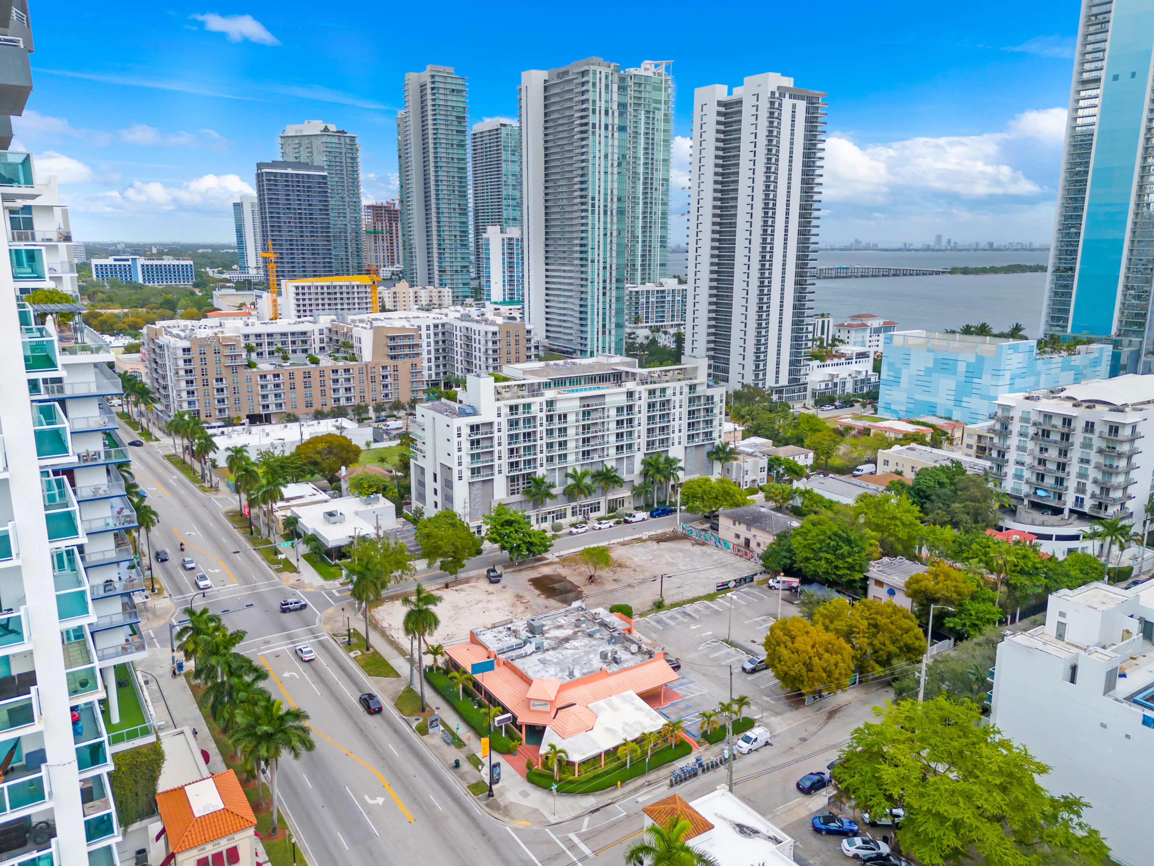 Aerial view of a cityscape featuring skyscrapers, residential buildings, and a roadway with sparse traffic, adjacent to a waterfront.